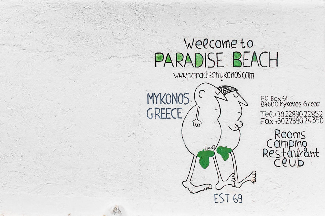 Paradise Beach, Mykonos, Greece - May 24th 2018: A painted sign welcomes visitors to Paradise Beach, advertising rooms, camping, a restaurant, and a club.