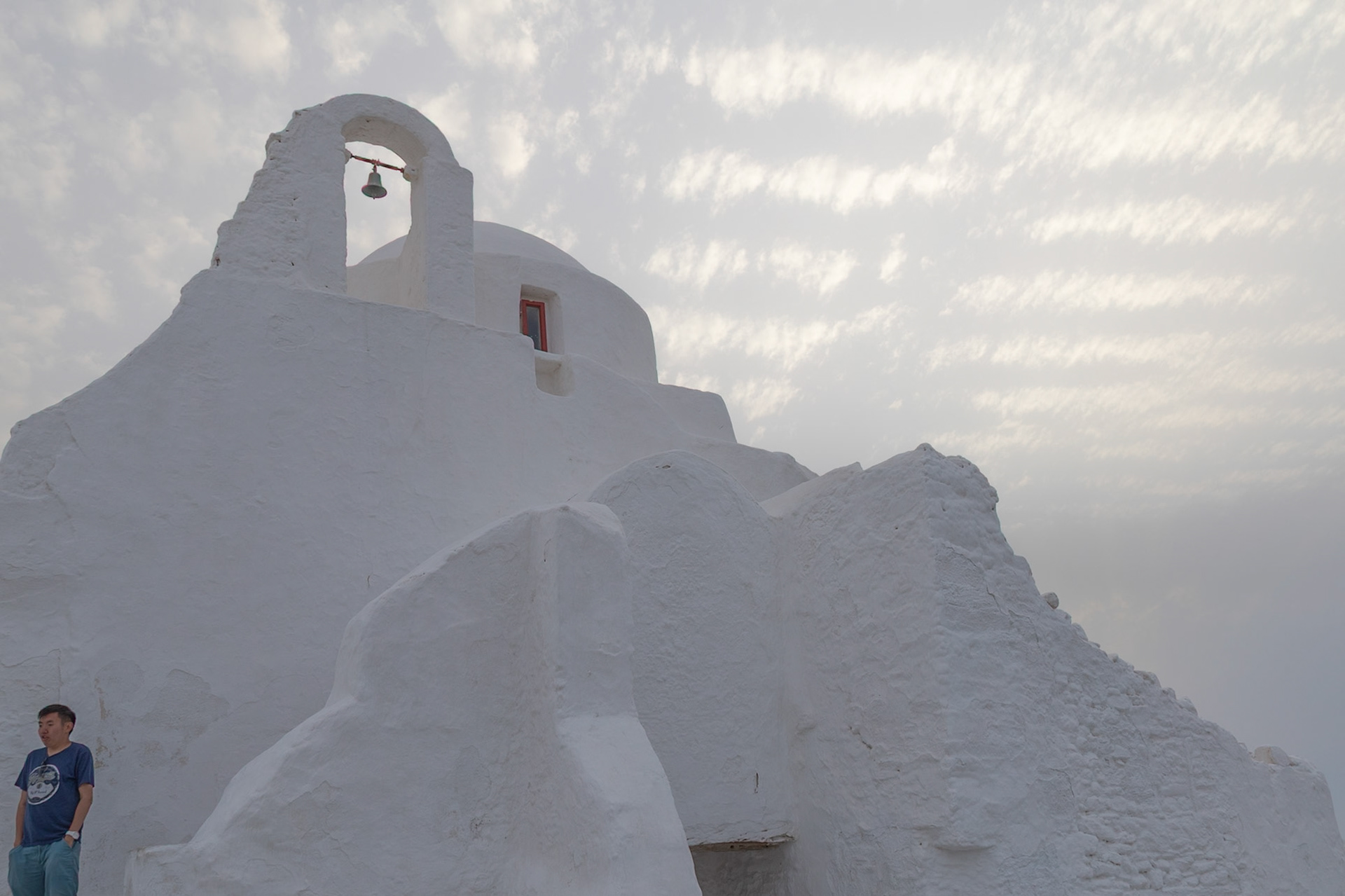 Mykonos, Greece - May 23rd 2018: A tourist admires the iconic whitewashed Paraportiani Church, a popular landmark on the island.