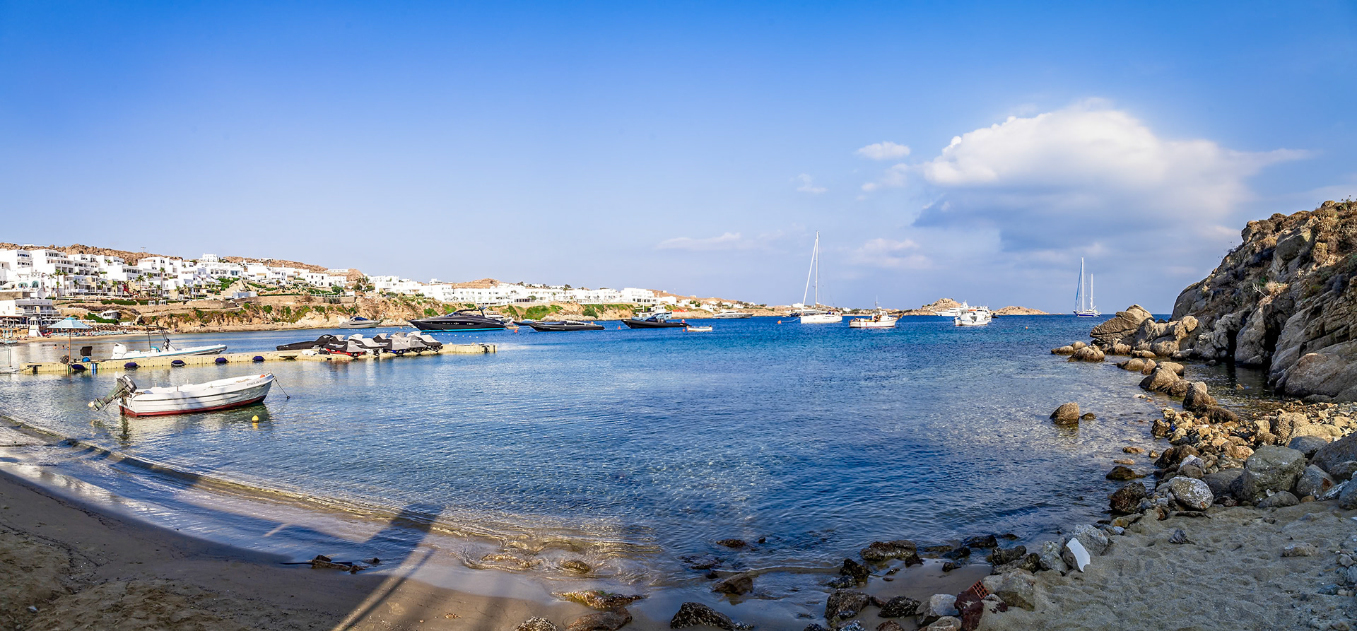 Psarou Beach, Mykonos, Greece - May 24th 2018: Boats are moored in the bay, with white buildings lining the coast, creating a scenic view.