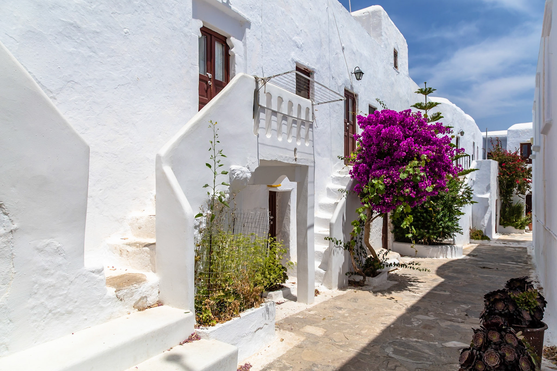 Mykonos, Greece - May 22nd 2018: A narrow street lined with white buildings and vibrant bougainvillea, showcasing the island's iconic architecture.