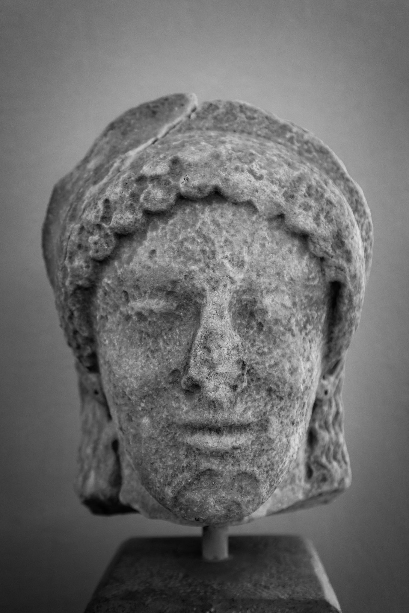 Delos, Greece - May 22nd 2018: A weathered marble head of a woman, possibly a goddess, is displayed. The statue's features are worn, hinting at its age and the passage of time.
