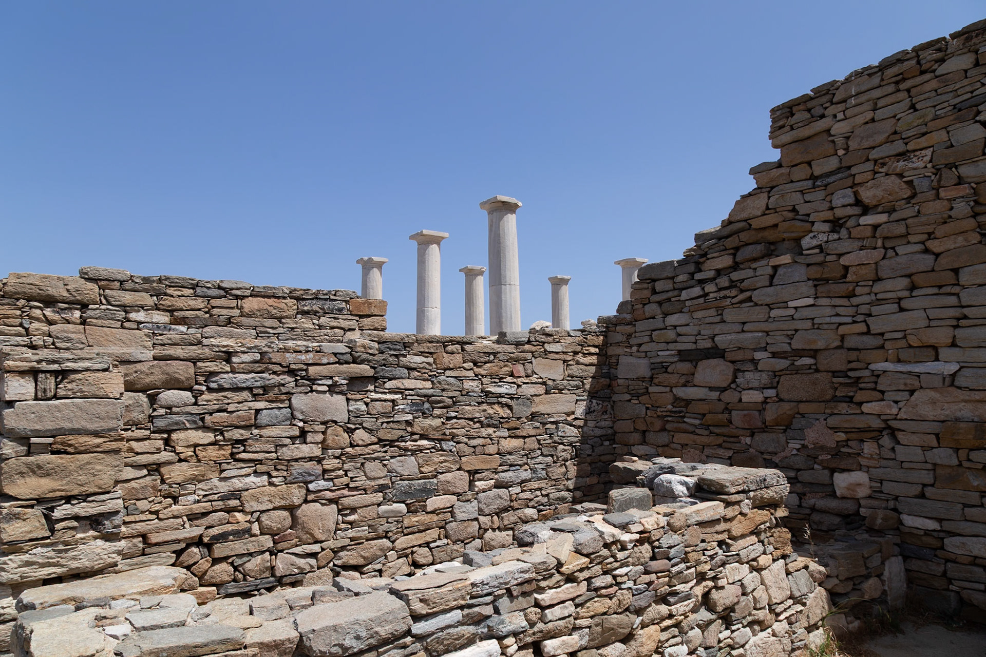 Delos, Greece - May 22nd 2018: Ruins of the ancient city of Delos, including stone walls and standing columns, are preserved as a historical site for visitors.