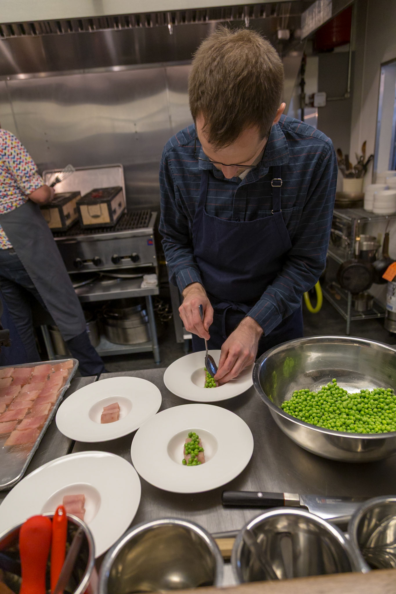 Fog Lark, Portland, Oregon - April 6th 2018: A chef plates a dish with peas and fish, ensuring each plate is perfect for the diners.