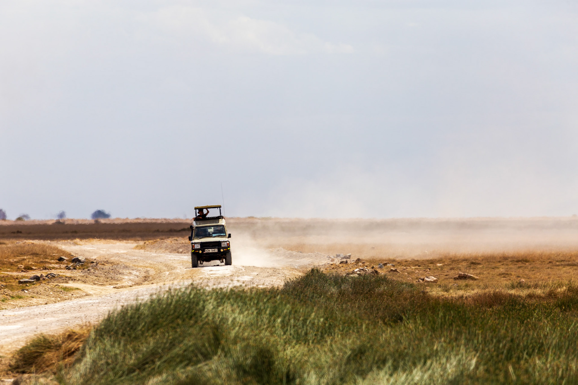 A safari vehicle drives through Amboseli National Park, Kenya, kicking up dust as tourists seek wildlife.