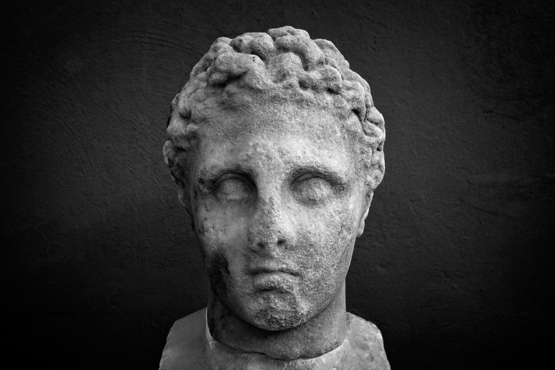 Delos, Greece - May 22nd 2018: A weathered marble head of a young man, possibly a god or hero, stands as a testament to ancient Greek artistry and culture.