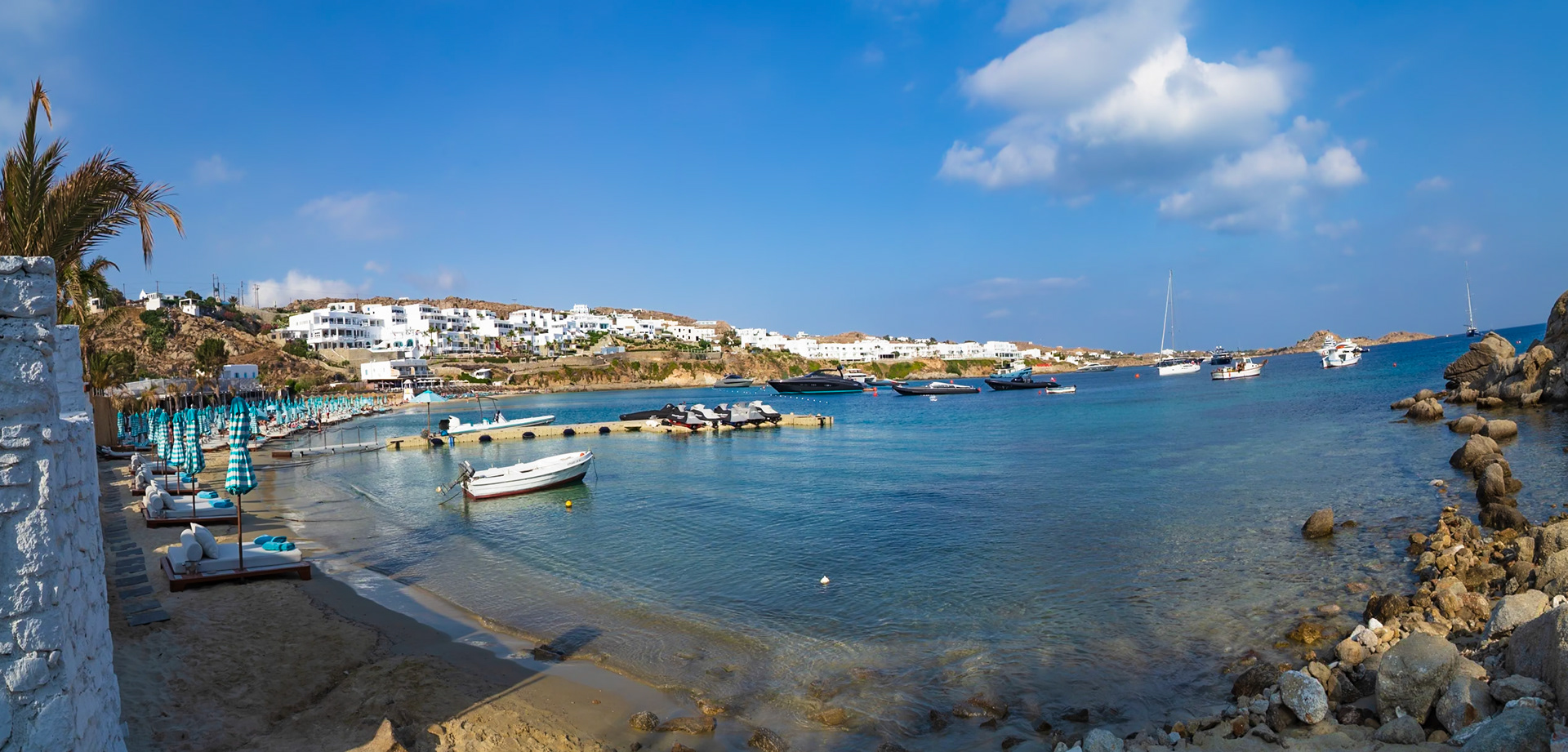 Psarou Beach, Mykonos, Greece - May 24th 2018: A scenic view of the beach with boats, jet skis, and beach umbrellas, showcasing the island's beauty.