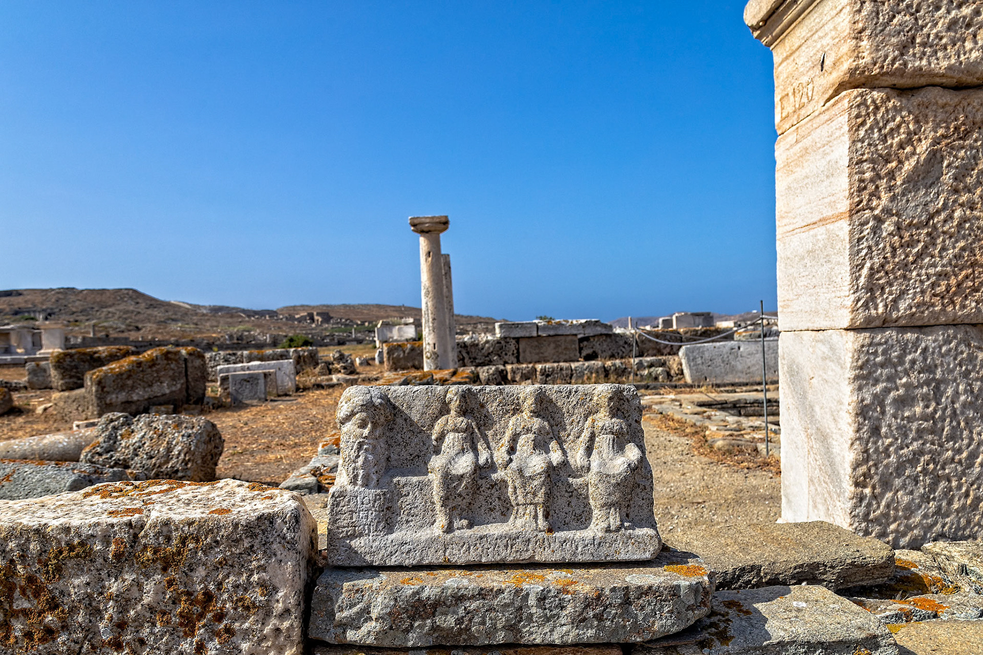 Delos, Greece - May 22nd 2018: An ancient stone carving of figures stands among the ruins of Delos, a UNESCO World Heritage site, showcasing the island's rich history.