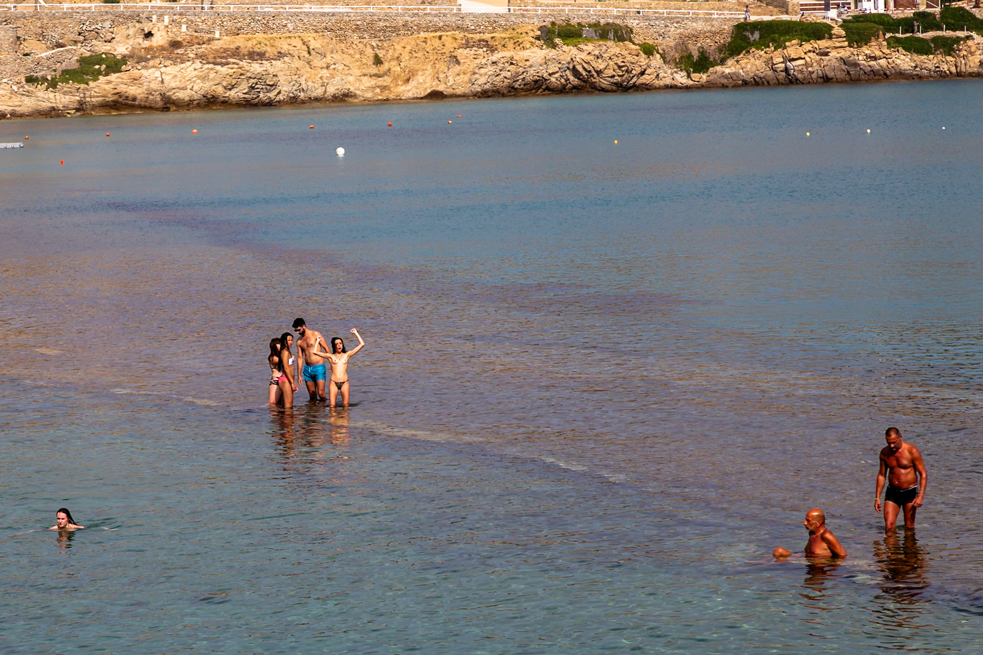 Paradise Beach, Mykonos, Greece - May 24th 2018: People are enjoying the clear, shallow water, swimming and standing in groups.