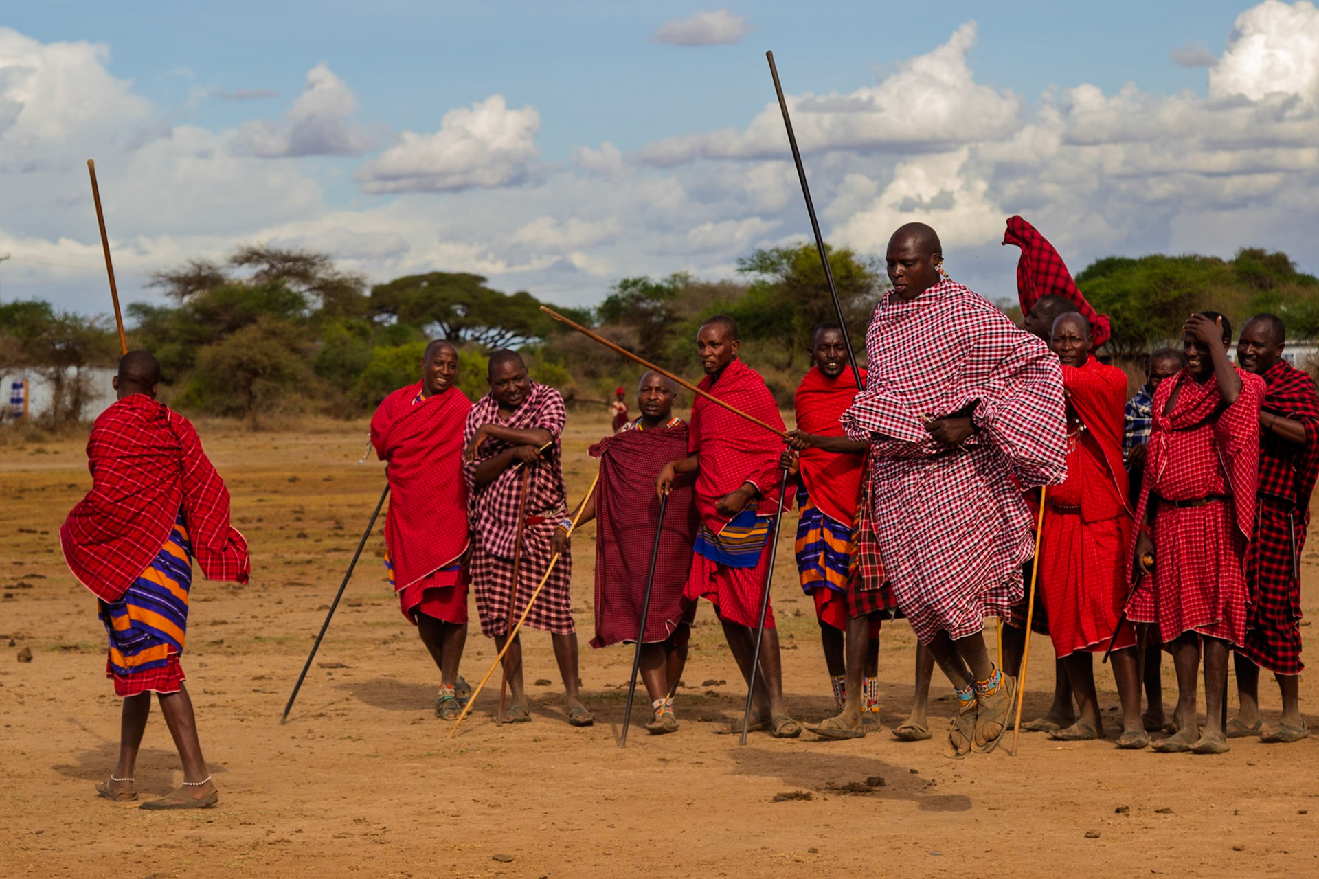 Maasai men in Kenya gather, clad in traditional red shukas and carrying staffs, showcasing their cultural heritage.