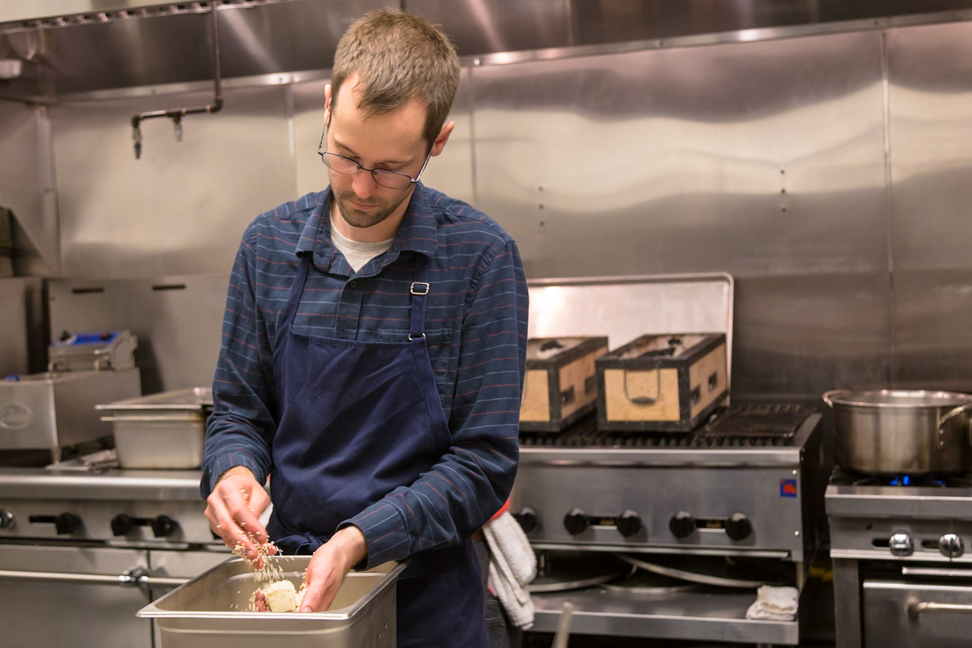 Fog Lark, Portland, Oregon - April 6th 2018: A chef prepares food in a commercial kitchen, coating it with sesame seeds.