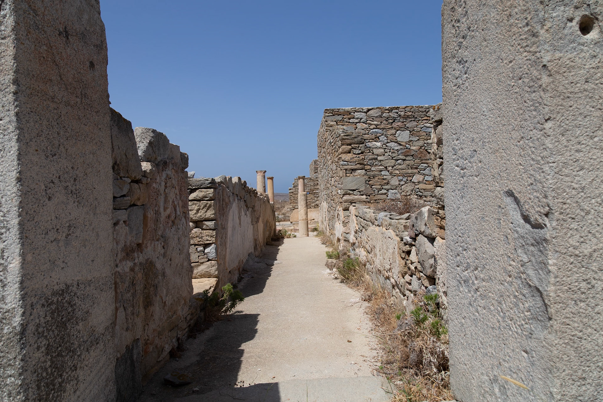 Delos, Greece - May 22nd 2018: A narrow path between ancient stone walls and ruins on the island of Delos, a UNESCO World Heritage site, showcasing its historical significance.