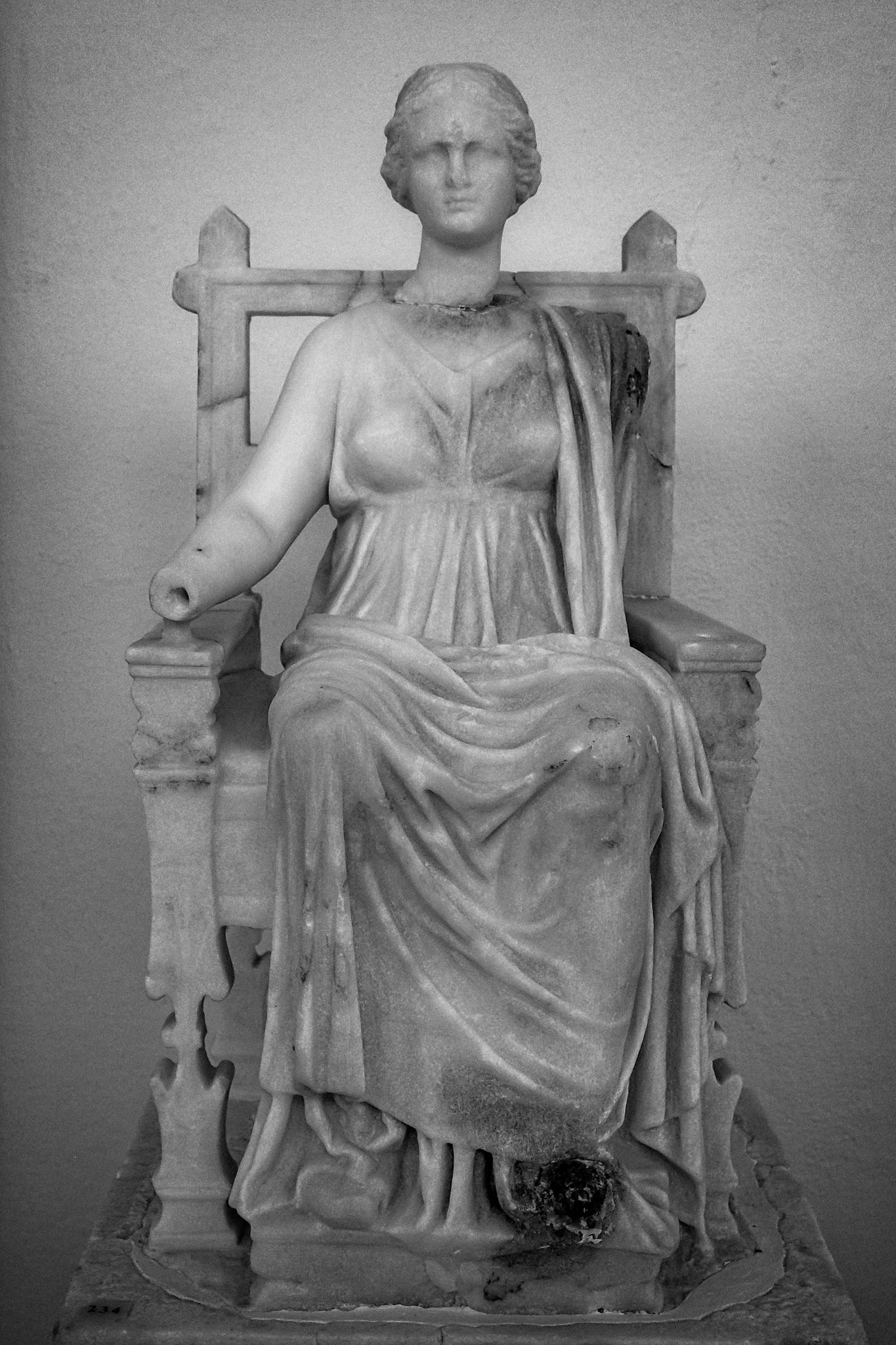 Delos, Greece - May 22nd 2018: A marble statue of a seated woman, possibly a goddess, is displayed. The statue is missing its head and arms, showing the wear of time.