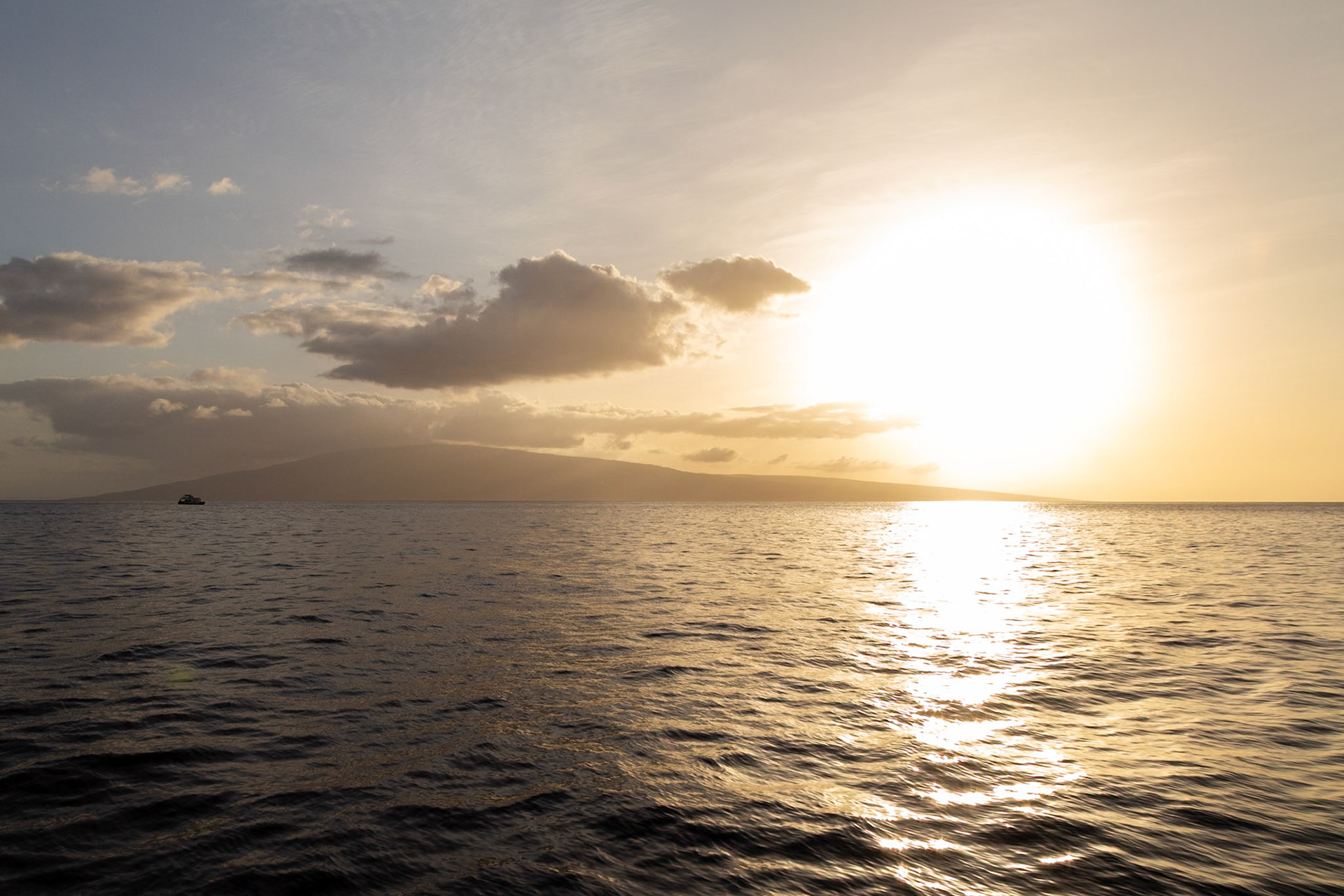 Maui, Hawaii, USA - April 7th 2022: A boat sails on the ocean as the sun sets, creating a golden glow over the water and the distant island.