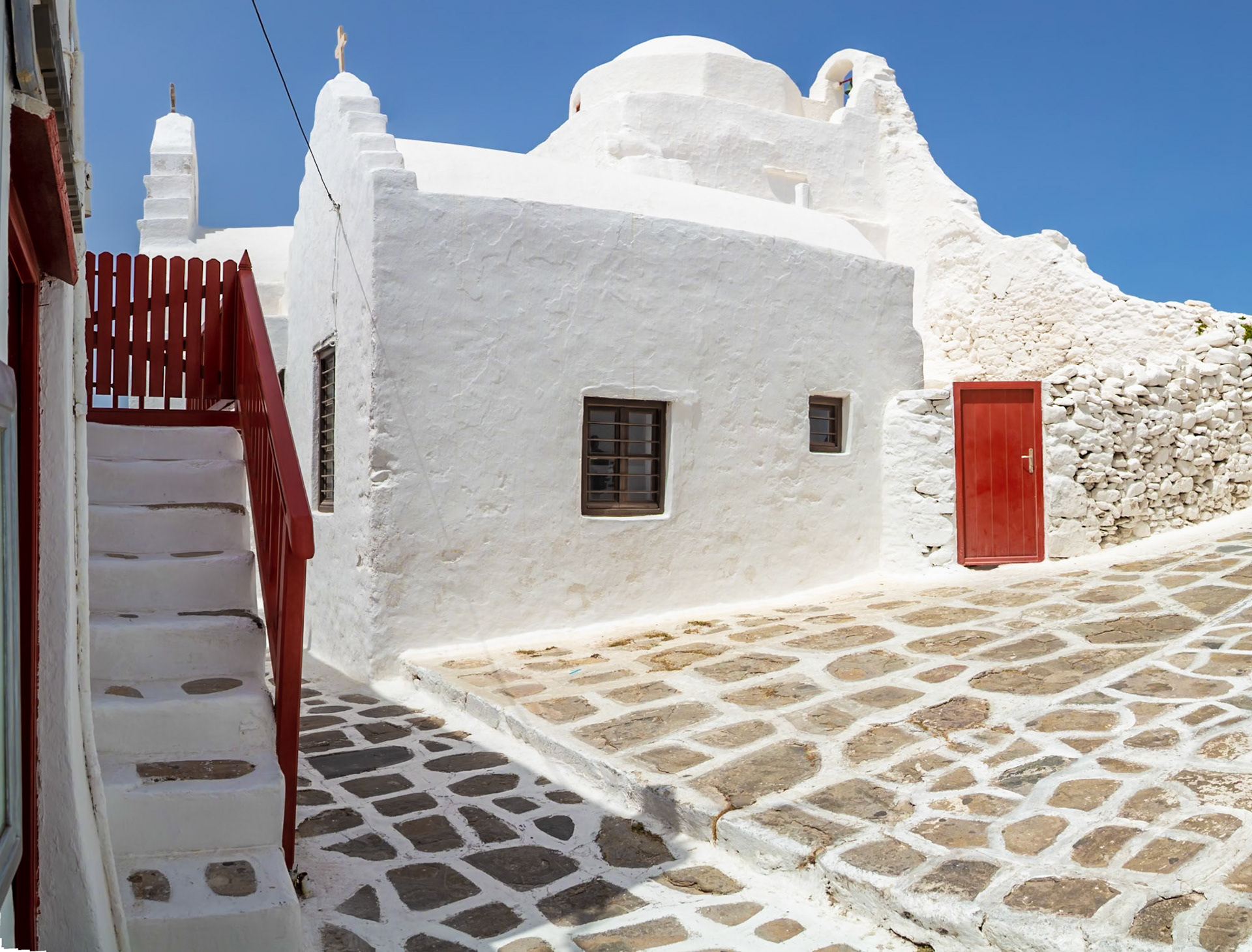 Mykonos, Greece - May 23rd 2018: A traditional whitewashed church stands on a stone-paved street, showcasing the island's iconic architecture.