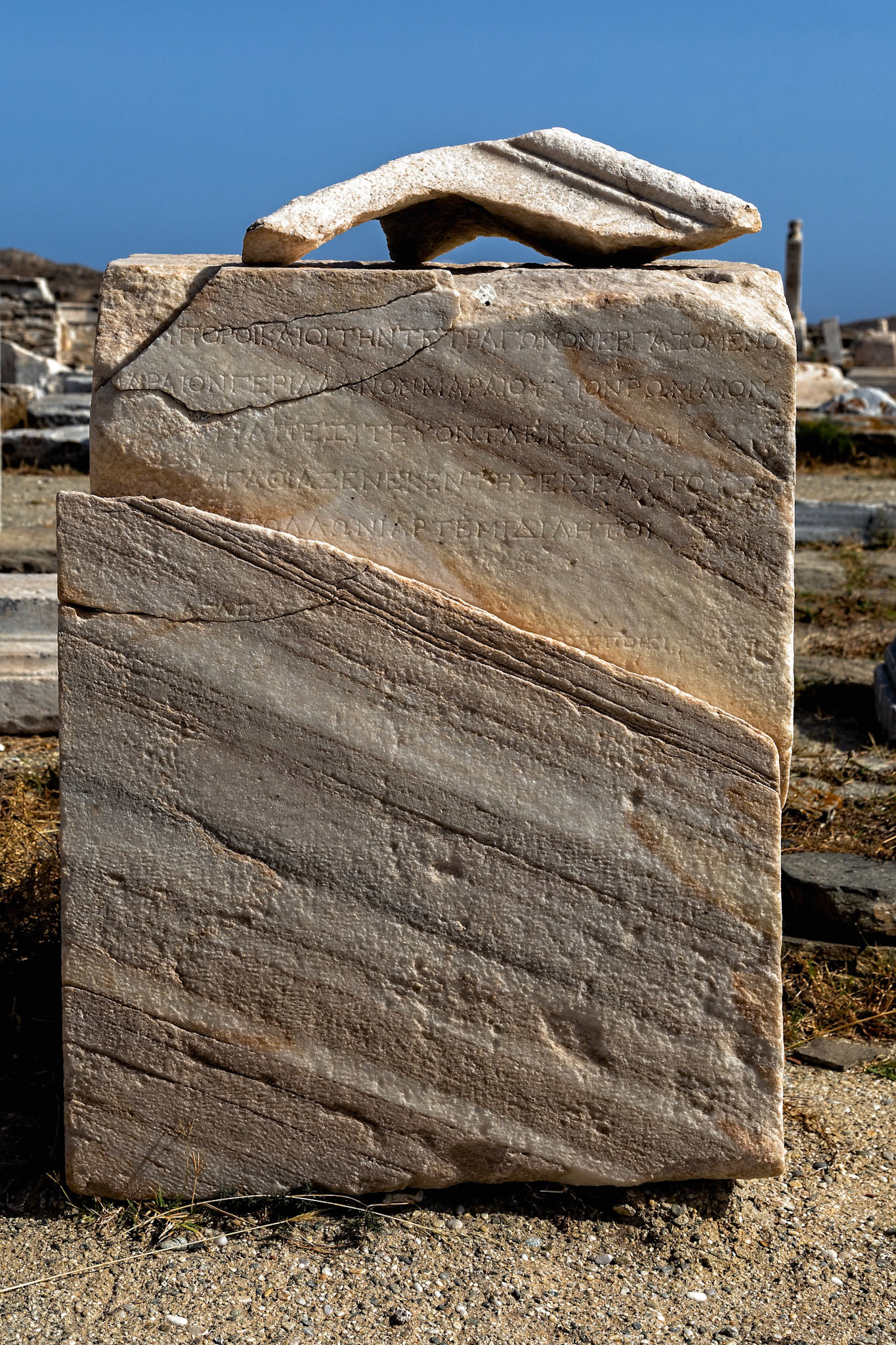 Delos, Greece - May 22nd 2018: An inscribed marble block lies in the archeological site. The inscriptions are in Greek, detailing historical or religious information.