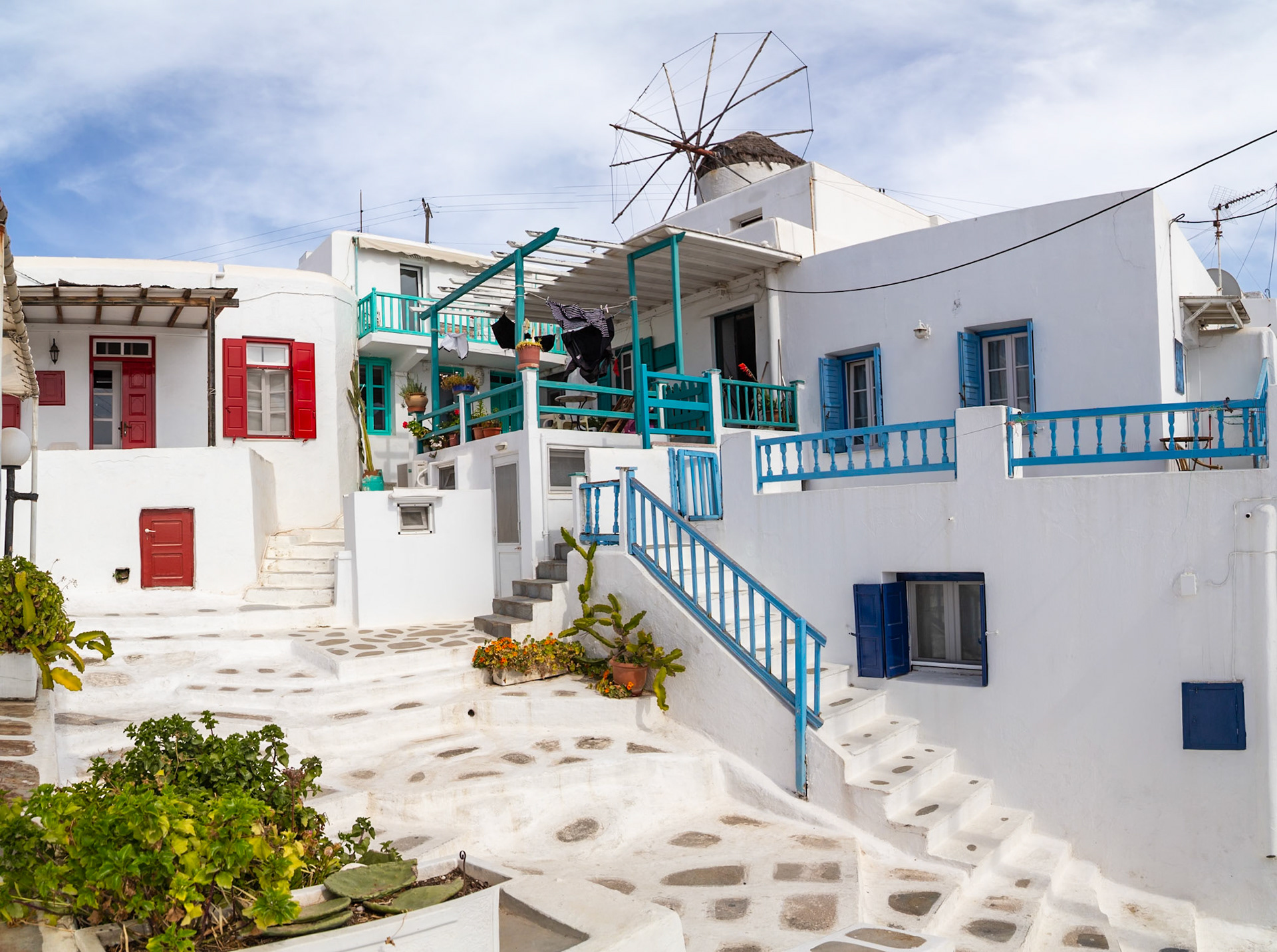 Mykonos, Greece - May 22nd 2018: Traditional white buildings with colorful accents and a windmill on a sunny day, showcasing Greek architecture.