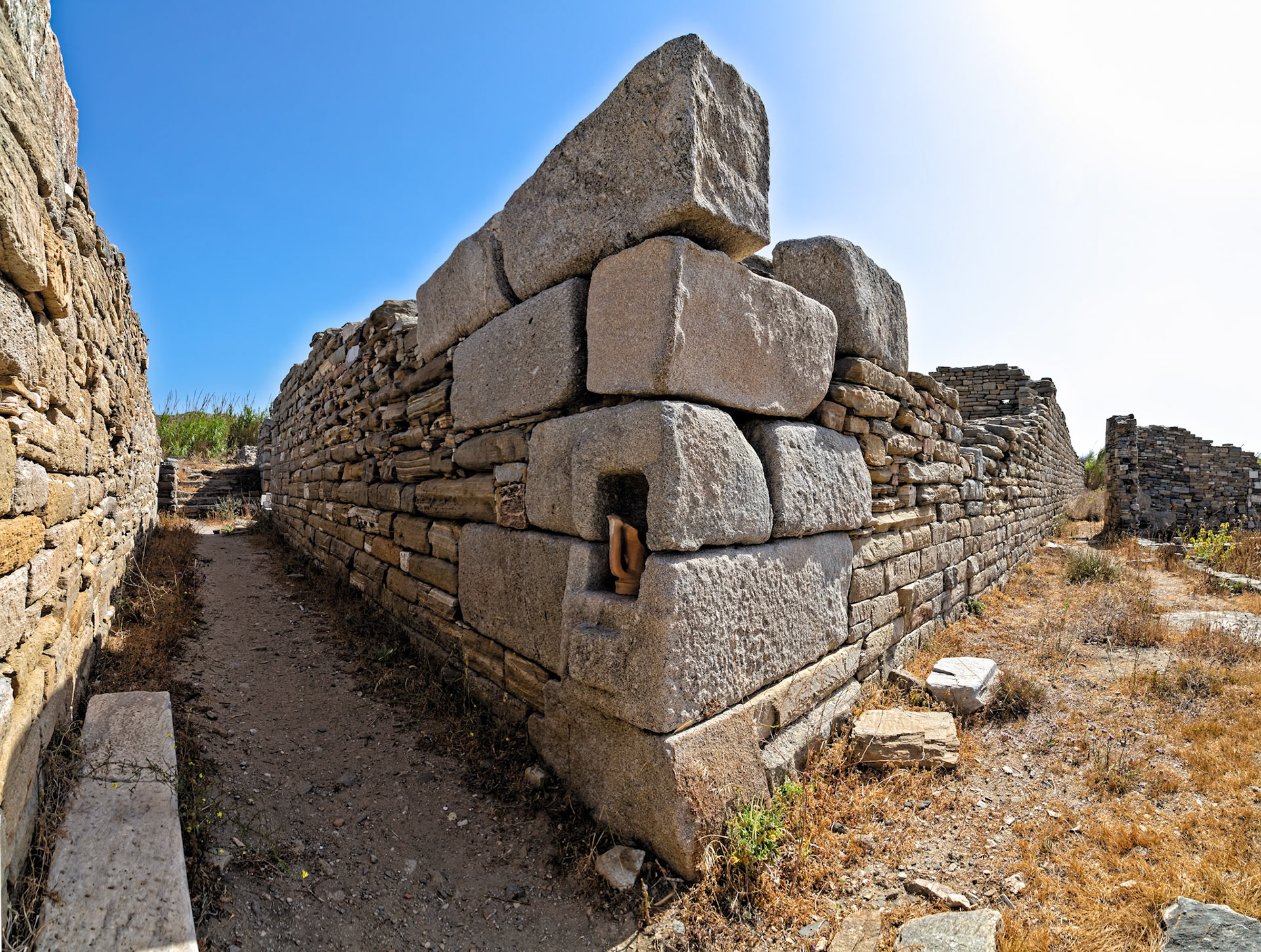 Delos, Greece - May 22nd 2018: Ancient stone walls stand tall, remnants of a bygone era. A clay pot sits in a niche, a silent witness to history.