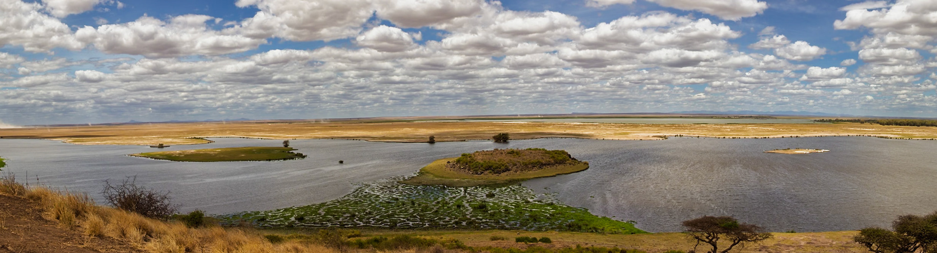 Panoramic view of Amboseli National Park, Kenya, showcasing the landscape with water, islands, and a cloudy sky.