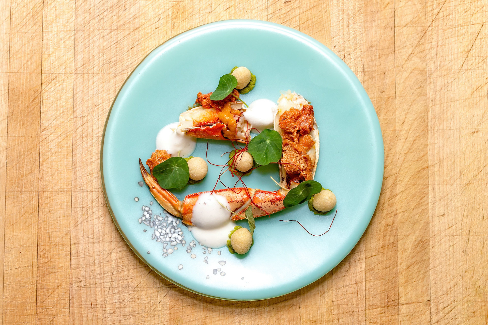 Fog Lark, Portland, Oregon - March 15th 2019: A culinary artist plates a Dungeness crab dish with foam, greens, and spheres for a fine dining experience.