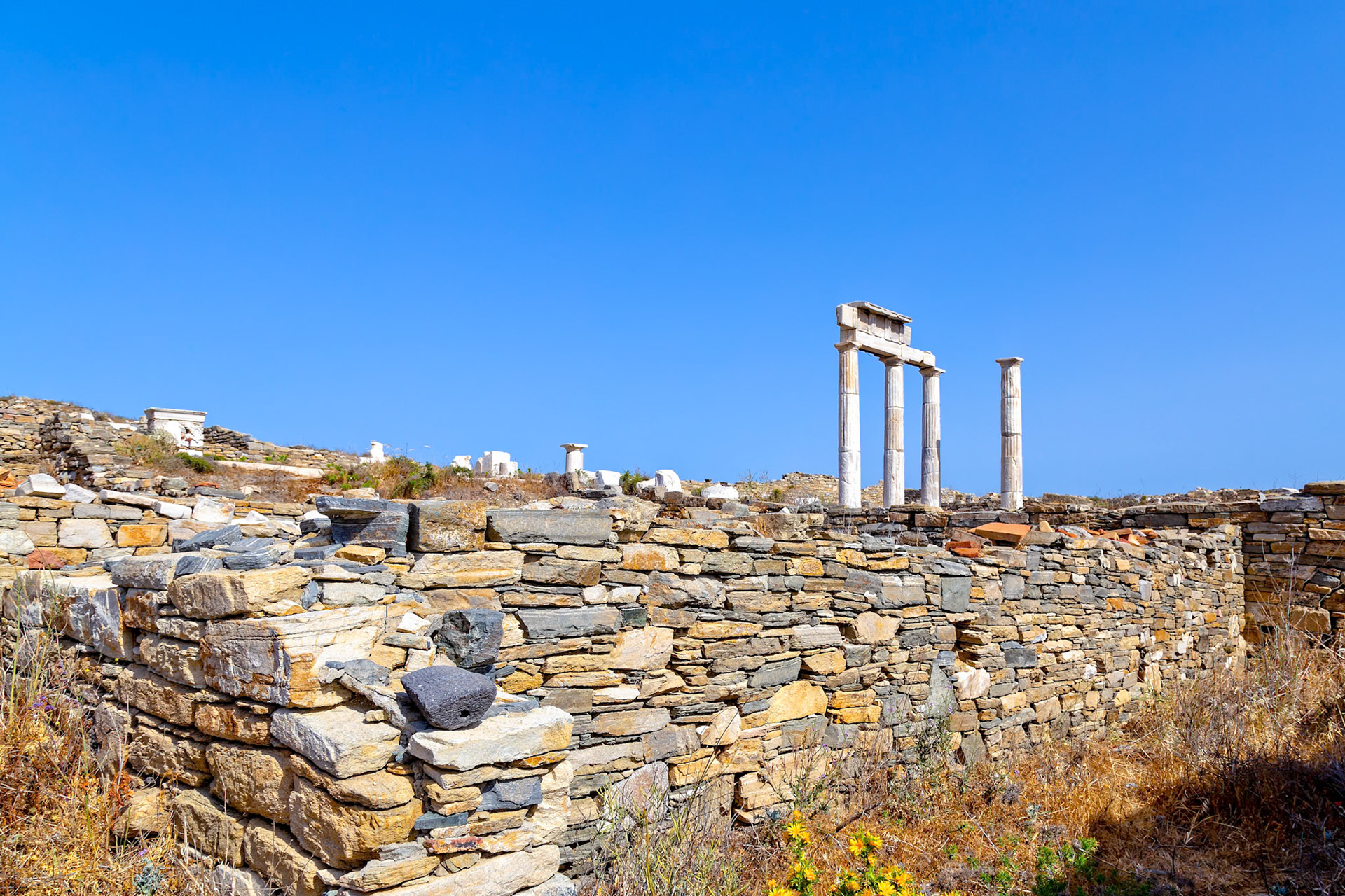 Delos, Greece - May 22nd 2018: Ancient ruins stand against a clear blue sky. The stone walls and columns are remnants of a once-thriving civilization.