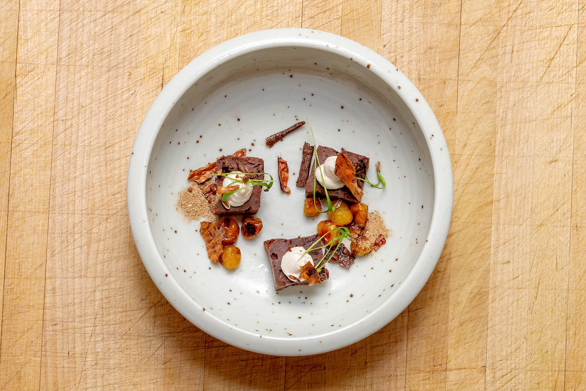 Fog Lark, Portland, Oregon - March 15th 2019: A chef plates a dessert featuring chocolate brownies, cream, and candied vegetables for a tasting menu.