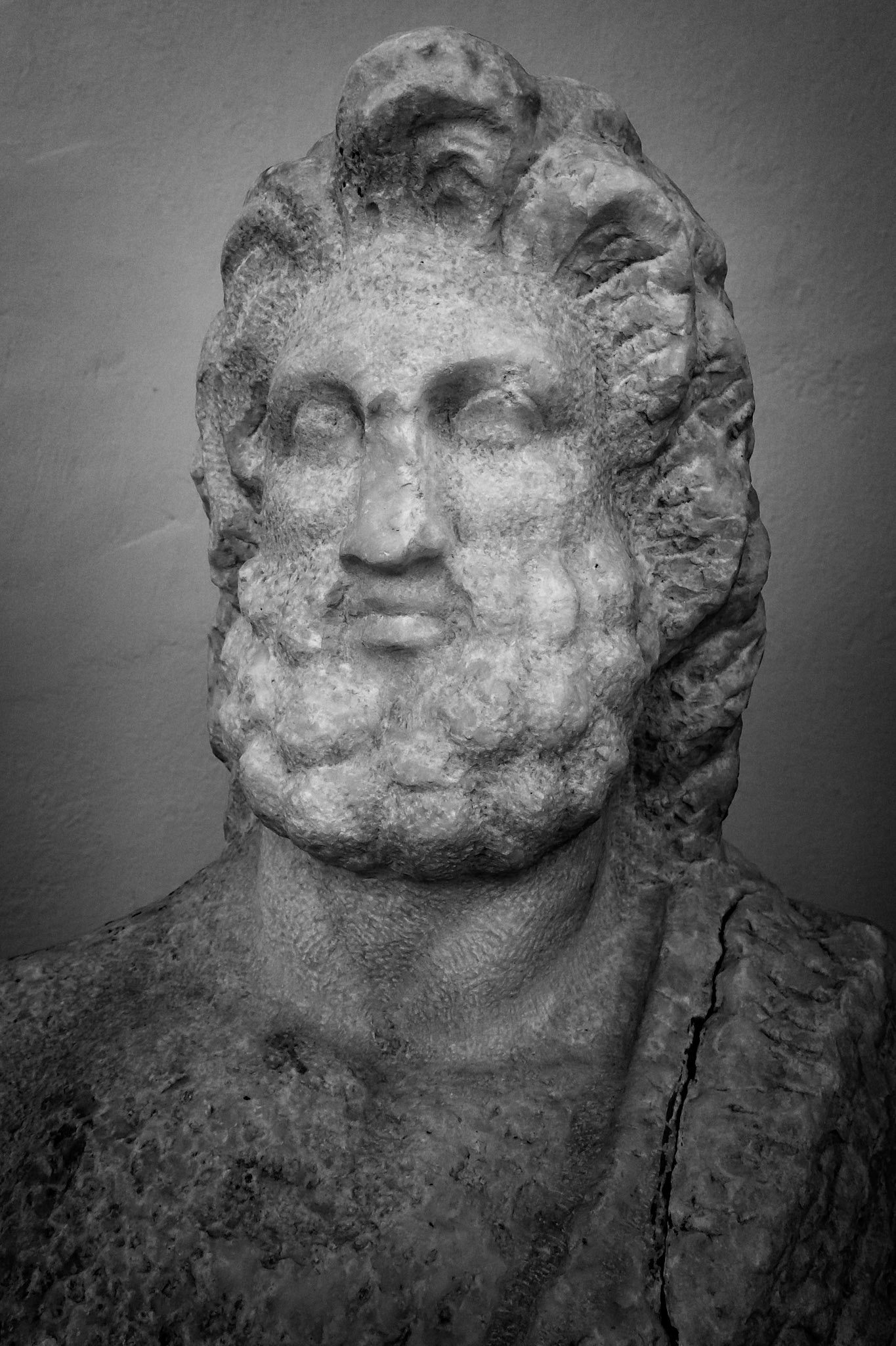 Delos, Greece - May 22nd 2018: A black and white close-up of a weathered marble bust of a bearded man, possibly a god or philosopher, on display at the archeological site.