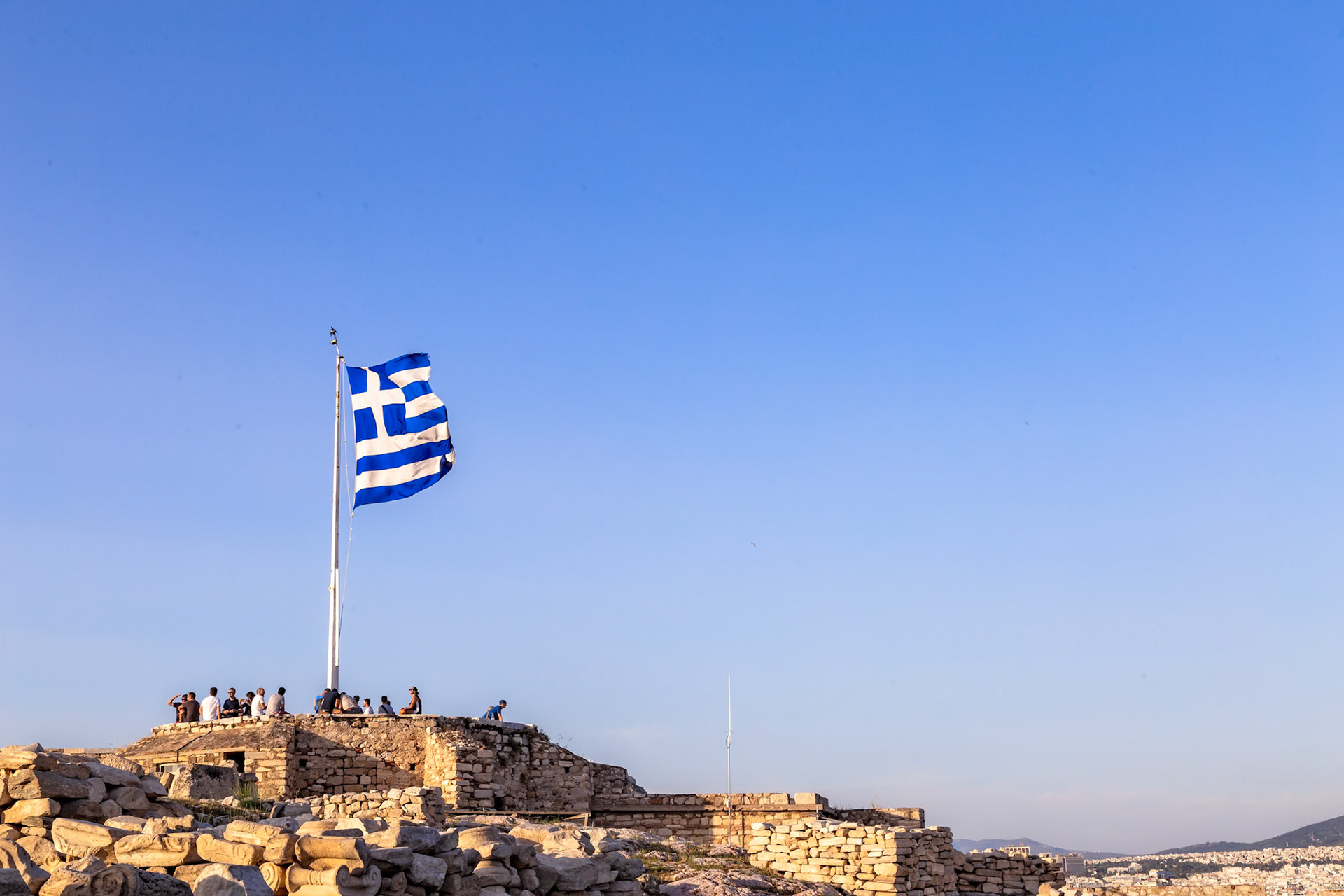 Acropolis, Athens, Greece - May 23rd 2018: Tourists gather atop the Acropolis, taking in the views and history, with the Greek flag waving proudly.