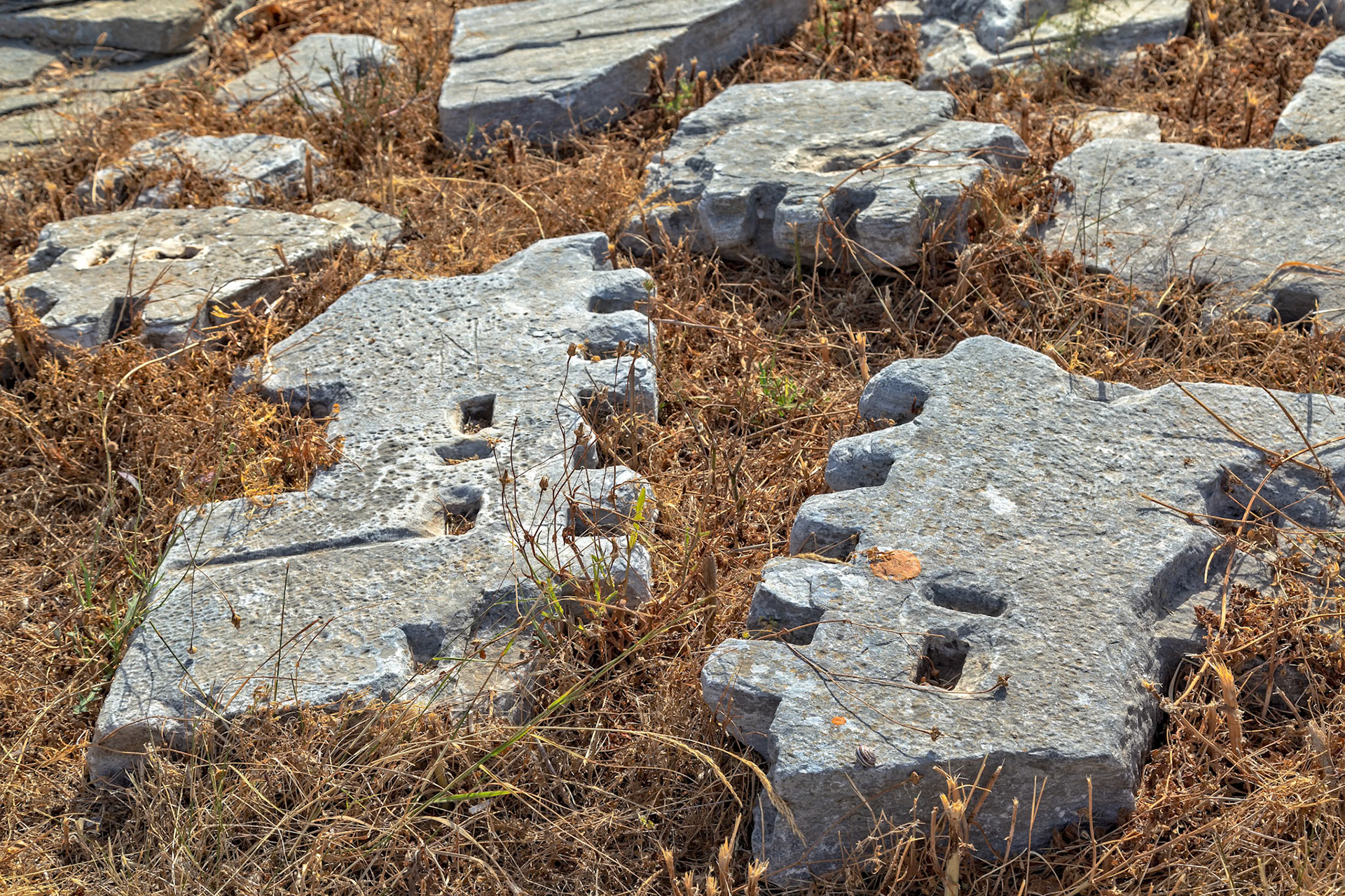 Delos, Greece - May 22nd 2018: Weathered stone ruins lay scattered among dry grass, remnants of an ancient civilization, showcasing the island's rich history.
