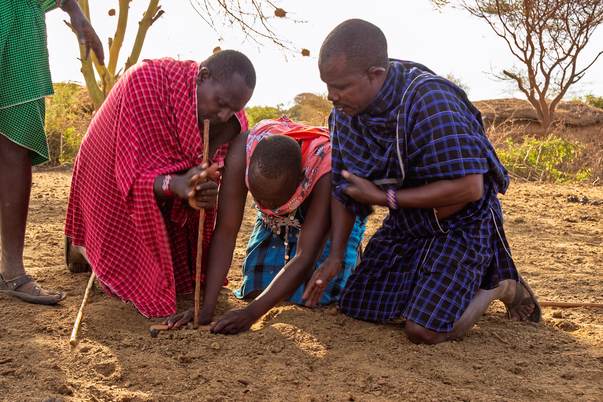 Maasai men in Kenya use traditional methods to start a fire in their village. They are using a stick and friction to create heat.