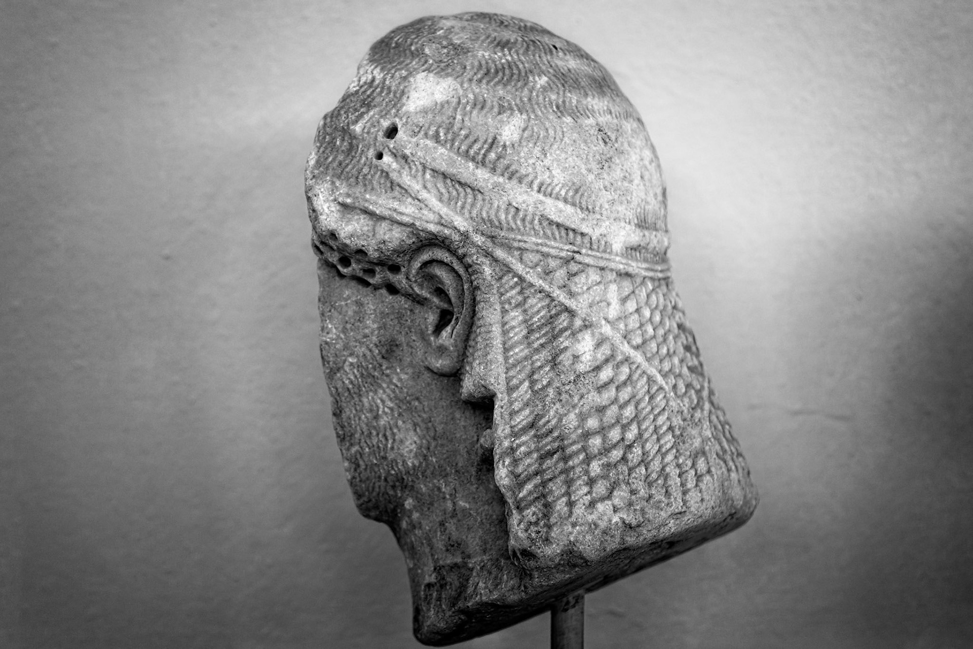 Delos, Greece - May 22nd 2018: A black and white close-up shows a weathered, ancient stone head sculpture, possibly a fragment of a larger statue, displayed on a stand.