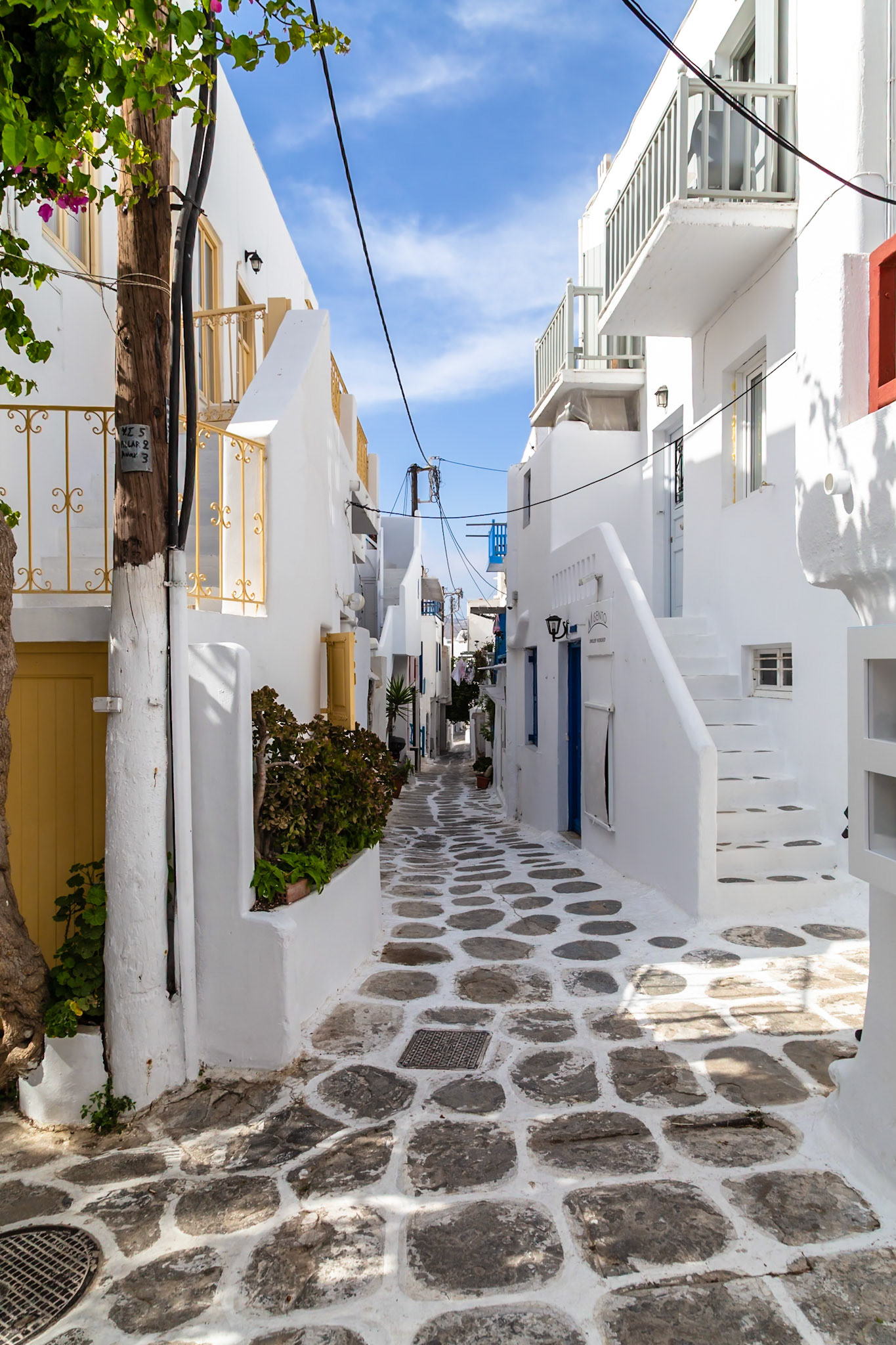 Mykonos, Greece - May 22nd 2018: A narrow street with white buildings and stone pavement, showcasing the island's traditional architecture.