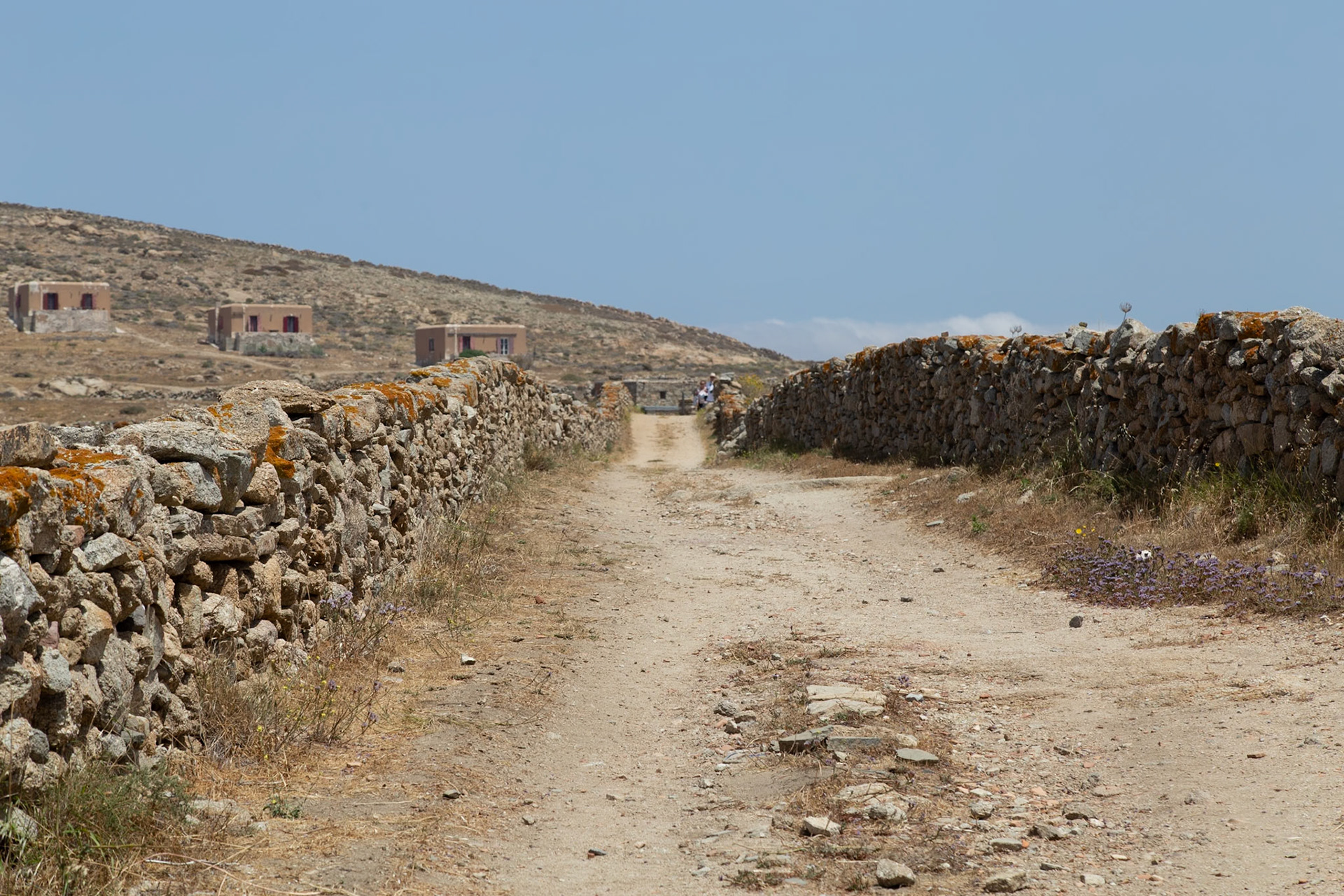 Delos, Greece - May 22nd 2018: Tourists explore the ancient ruins of Delos, walking along a path lined with stone walls, discovering the island's rich history.