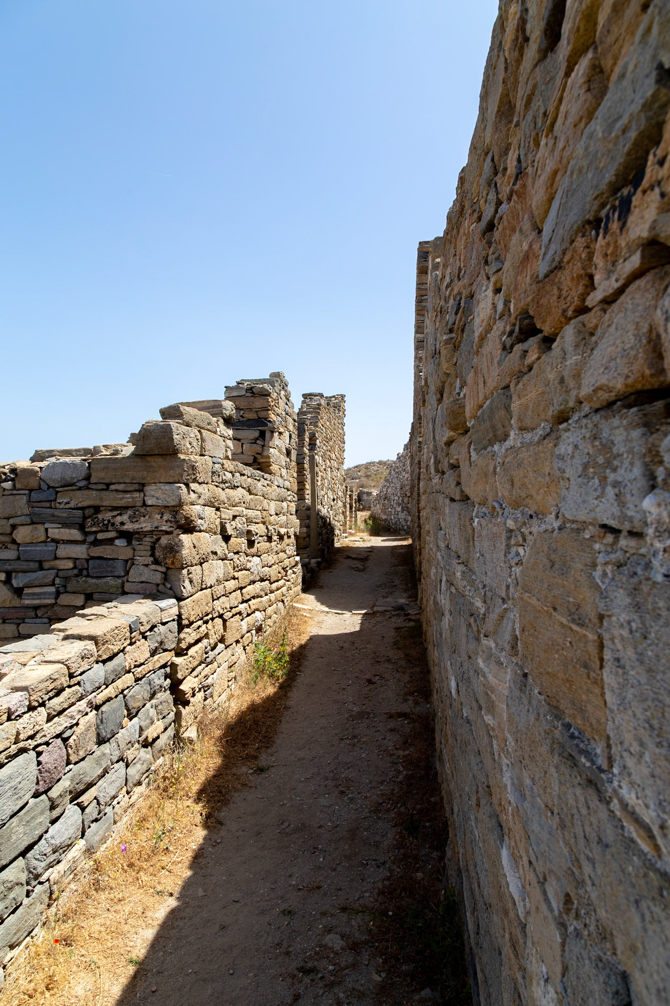 Delos, Greece - May 22nd 2018: A narrow path between ancient stone walls on the island of Delos, a UNESCO World Heritage site, showcasing the ruins of a once-thriving port city.