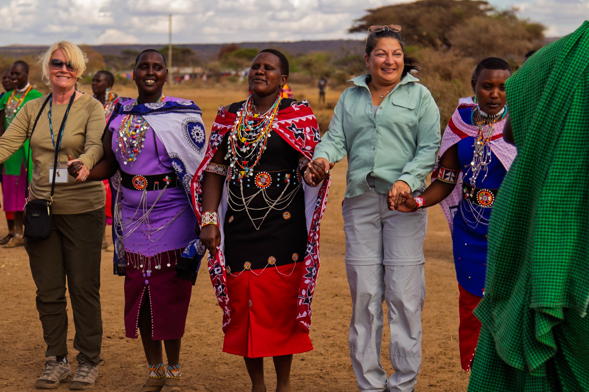 Tourists visit a Maasai village in Kenya, joining hands with Maasai women in traditional dress, experiencing their culture.