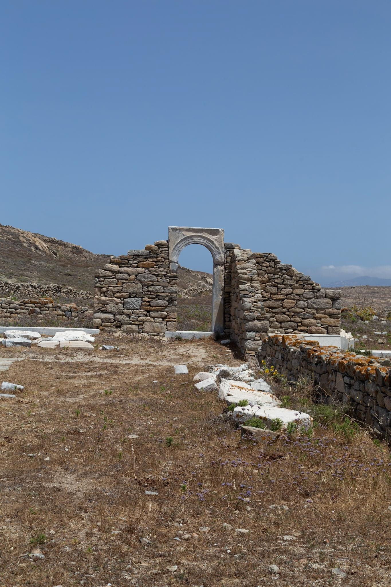 Delos, Greece - May 22nd 2018: Ruins of an ancient structure stand against a clear sky. The stone archway and walls evoke the island's rich history and cultural significance.