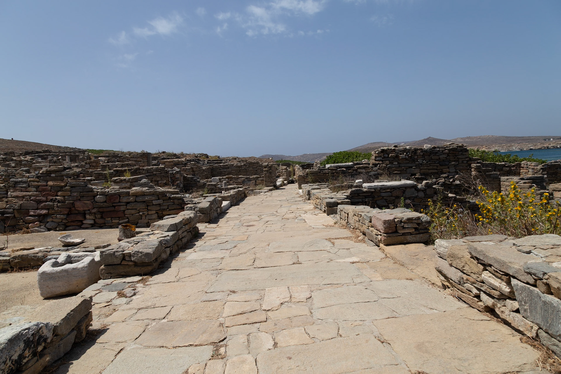Delos, Greece - May 22nd 2018: A stone path leads through the ruins of Delos, a significant archaeological site. The path is lined with stone walls and remnants of ancient structures.