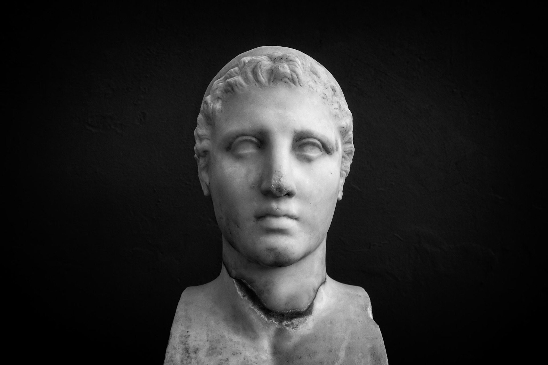 Delos, Greece - May 22nd 2018: A marble bust of a person with short curly hair, likely a historical figure, is displayed against a dark background.