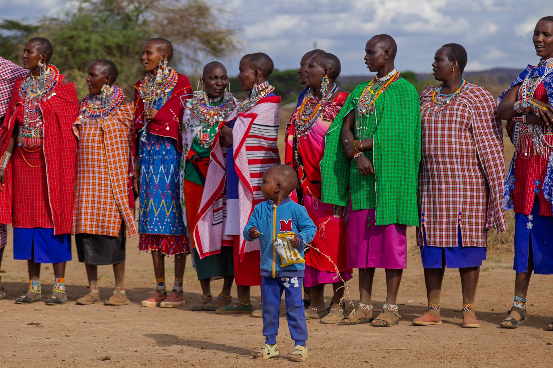 A group of Maasai women in Kenya stand together in traditional dress, while a child stands in front of them.