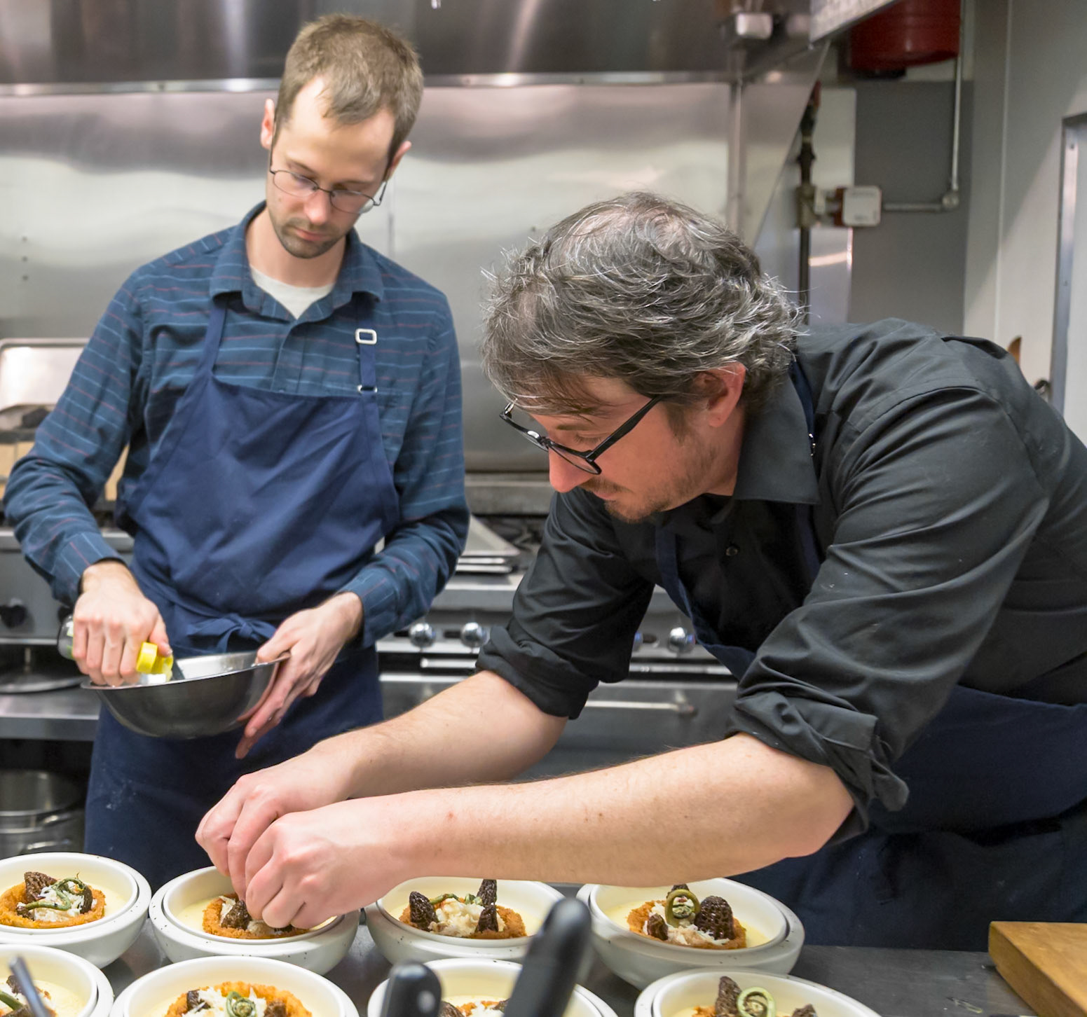 Fog Lark, Portland, Oregon - April 6th 2018: Two chefs plating dishes in a professional kitchen, adding garnishes for a visually appealing presentation.
