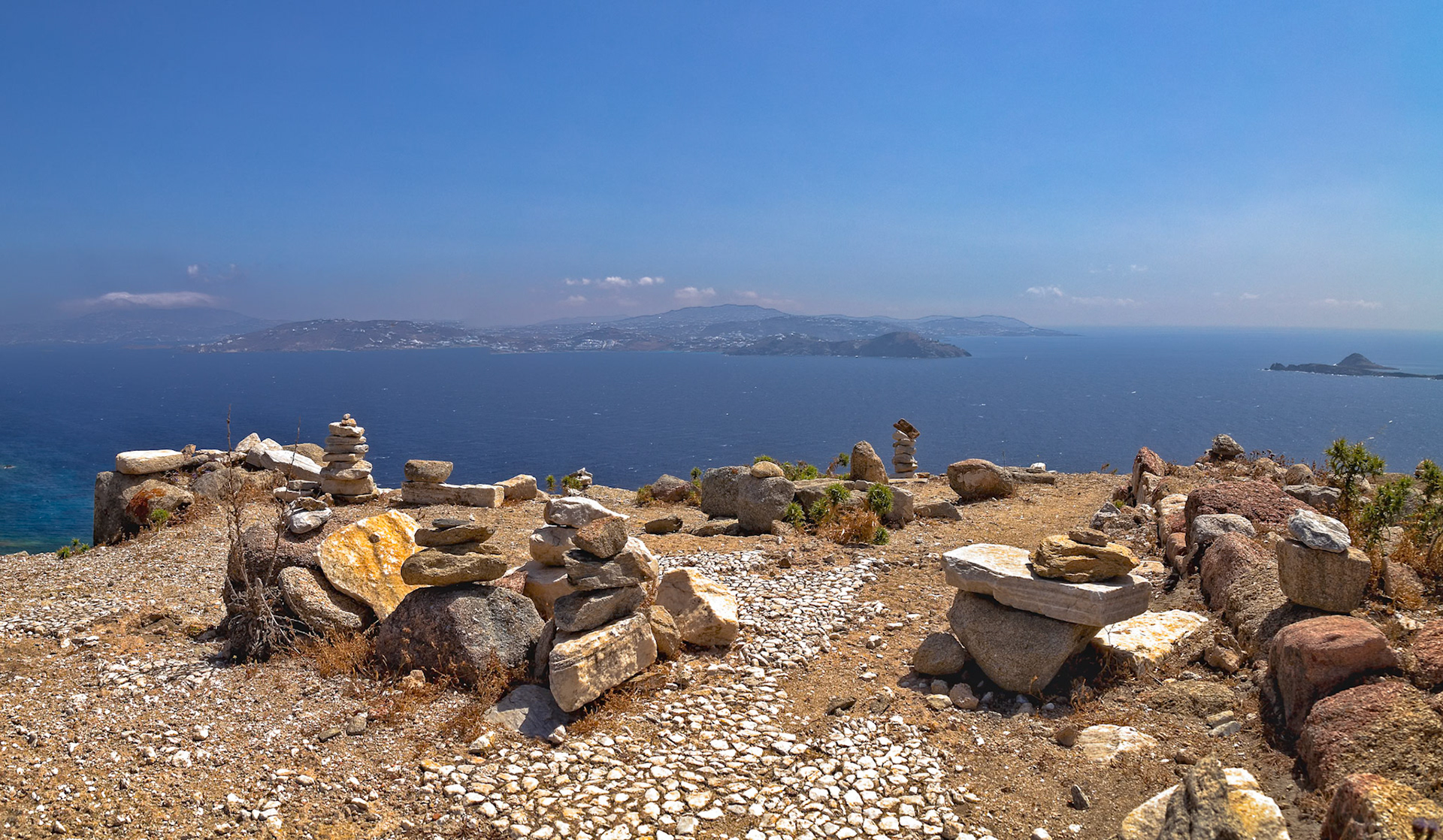 Delos, Greece - May 22nd 2018: Rock cairns stand on Delos, overlooking the Aegean Sea. These structures are built by visitors, adding to the island's unique landscape.