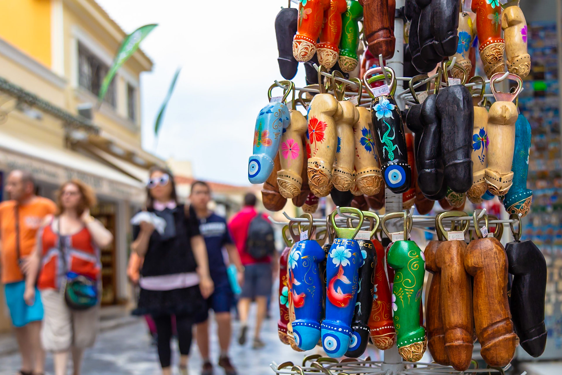 Athens, Greece - May 23rd 2018: Tourists stroll past a souvenir stand selling phallic-shaped bottle openers, a common sight in Greek tourist areas.