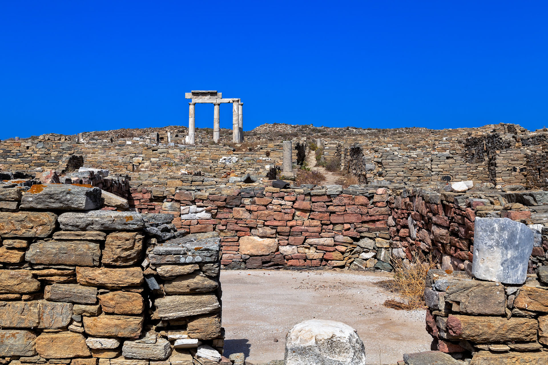 Delos, Greece - May 22nd 2018: Ruins of ancient stone structures stand against a clear blue sky, showcasing the historical architecture of Delos.