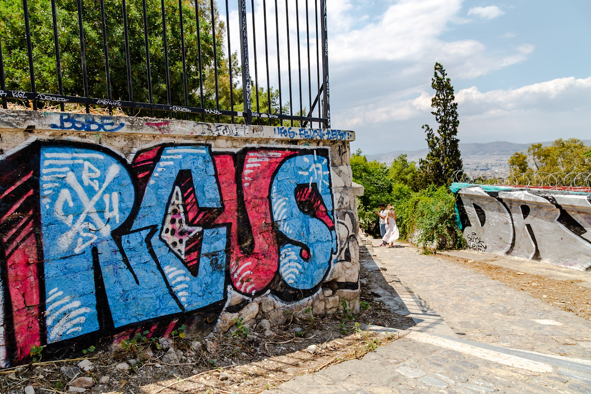 Athens, Greece - May 23rd 2018: A couple strolls along a graffiti-covered path, possibly exploring the city or enjoying a leisurely walk.