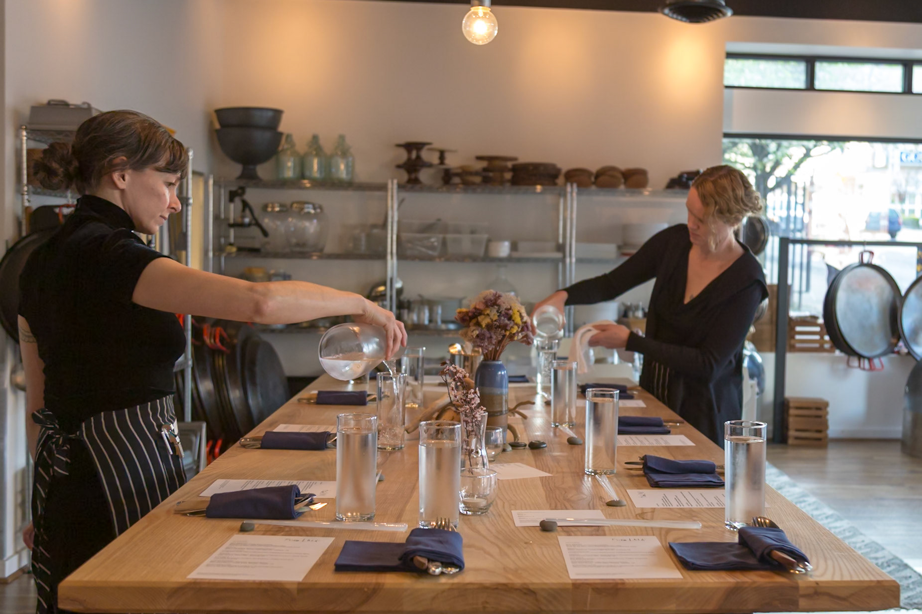 Fog Lark, Portland, Oregon - April 6th 2018: Two servers prepare a long table for a dinner service, pouring water and polishing glasses.