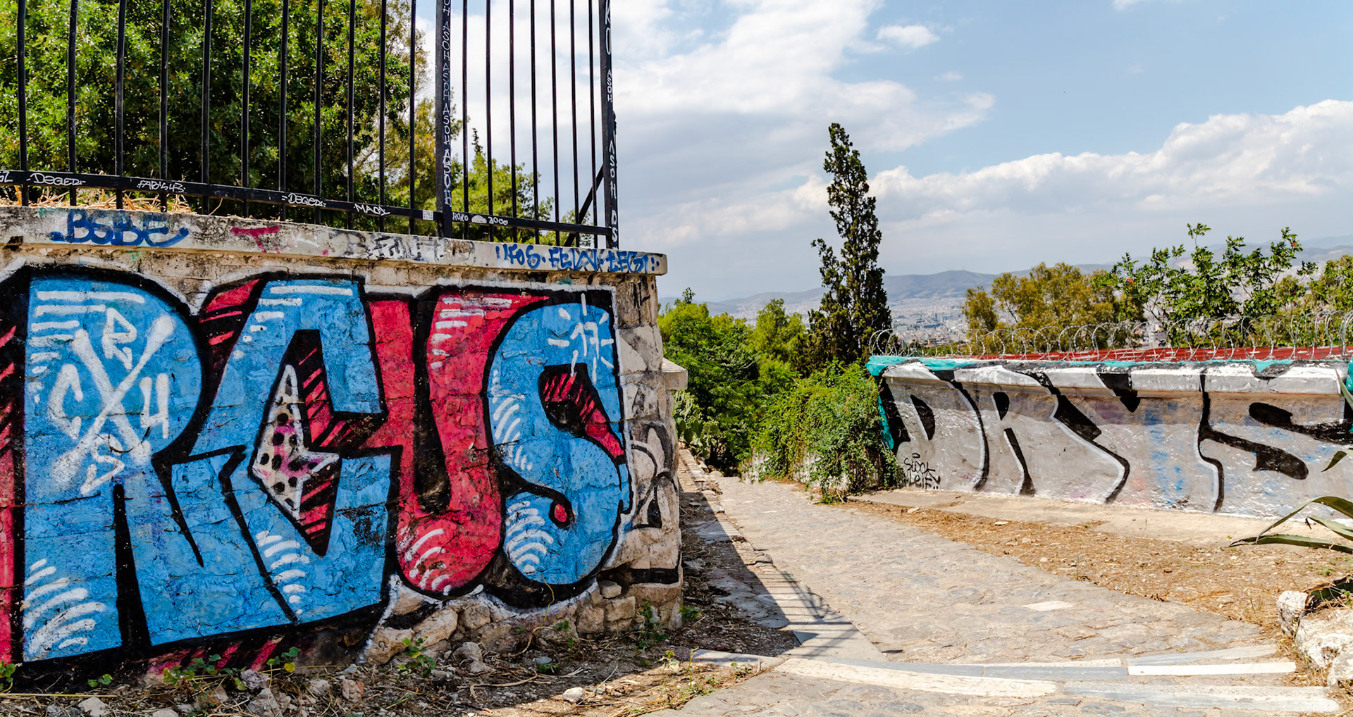Athens, Greece - May 23rd 2018: Graffiti art adorns a stone wall along a path, showcasing urban expression and adding color to the city's landscape.
