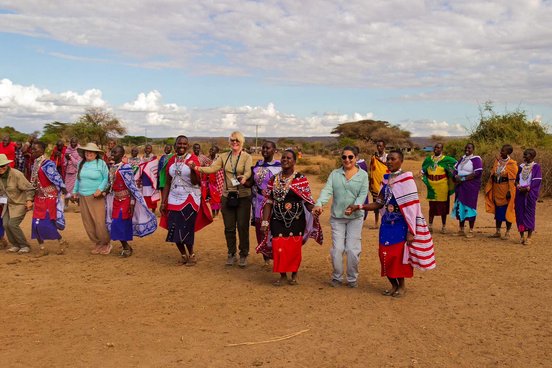 Tourists join Maasai women in a traditional dance in their village in Kenya, experiencing local culture.