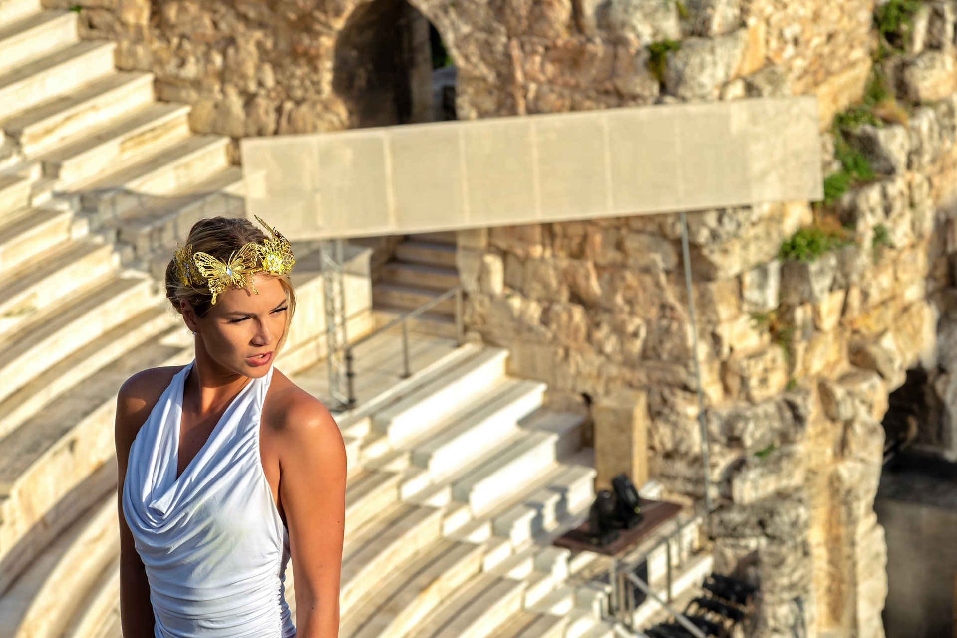 Acropolis, Athens, Greece - May 23rd 2018: A woman in a white dress and butterfly crown poses at the Odeon of Herodes Atticus, likely for a photoshoot.