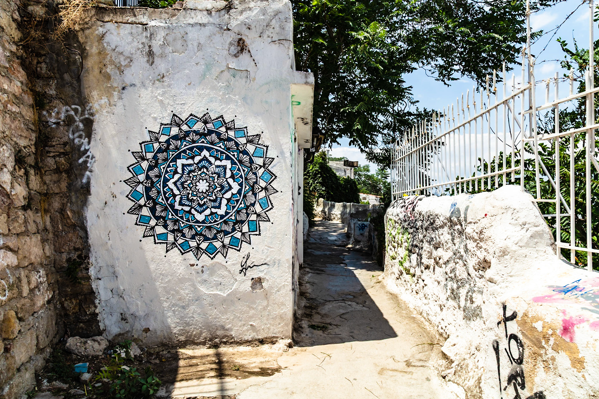 Athens, Greece - May 23rd 2018: A narrow alleyway is decorated with street art, including a blue mandala, adding color and character to the urban landscape.