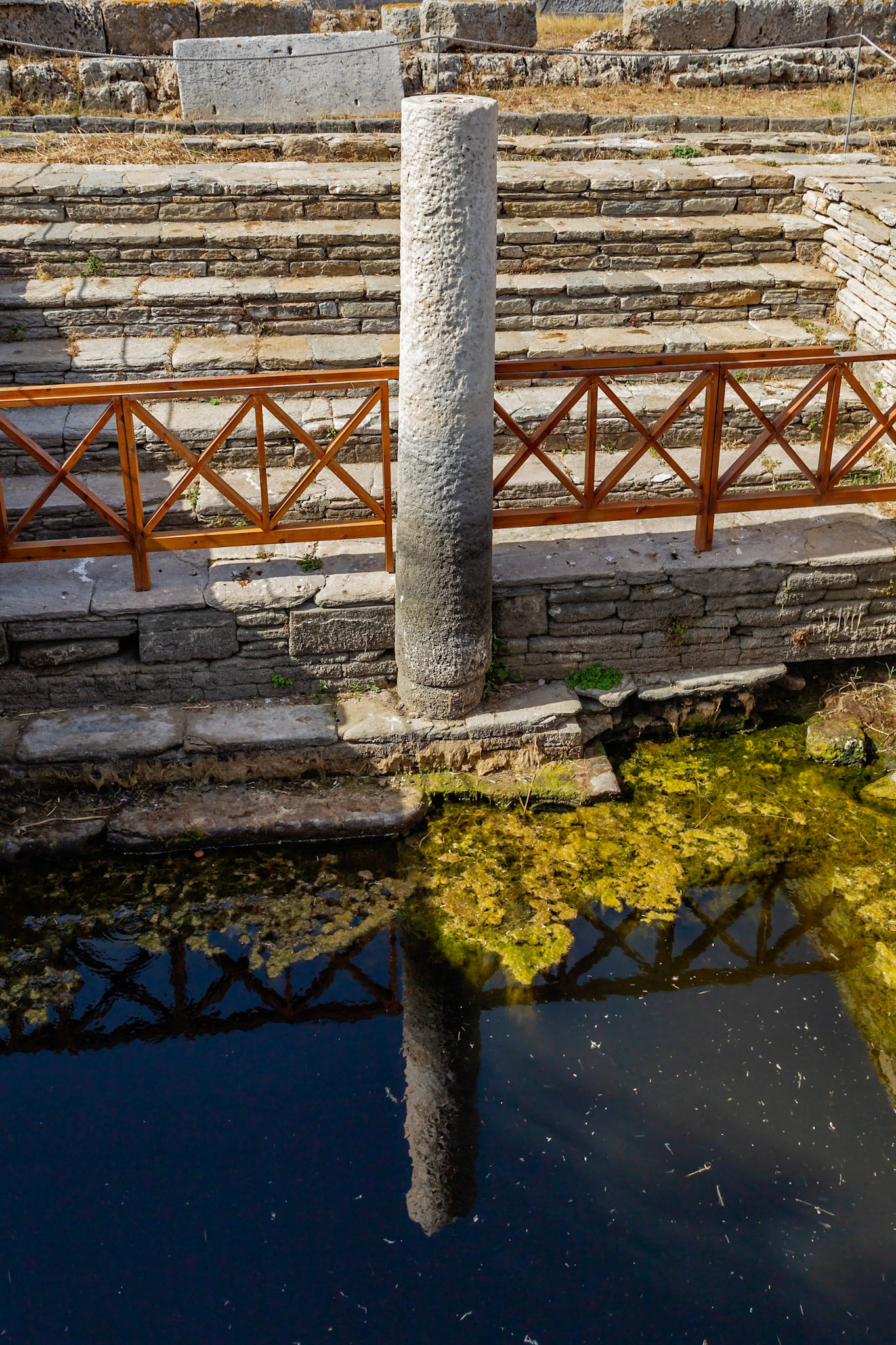 Delos, Greece - May 22nd 2018: A pillar stands in the Pool of Purification, an ancient structure used for religious cleansing on the island of Delos.