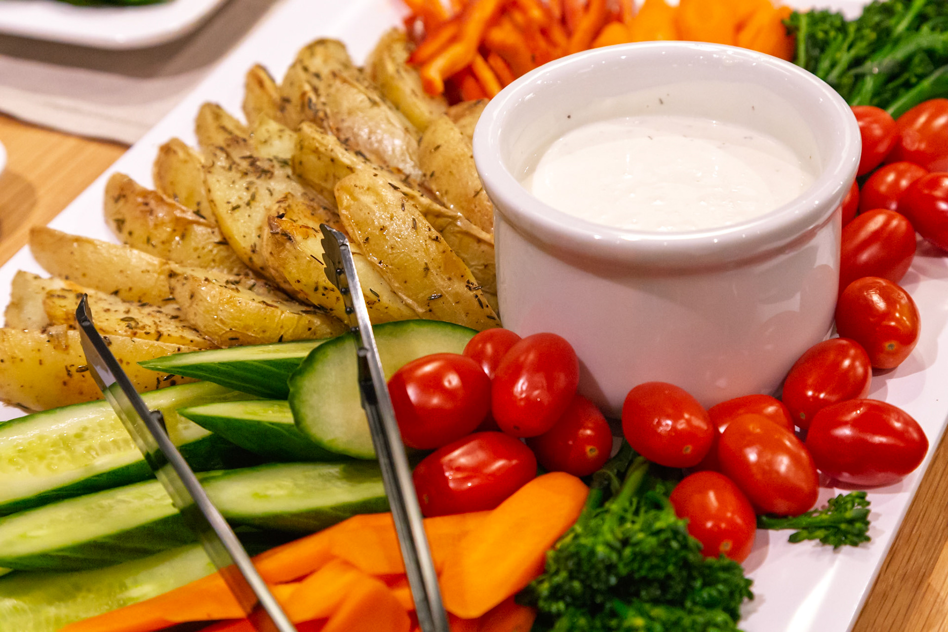 A platter of roasted potato wedges, fresh vegetables, and dip is ready to be served at a party or gathering.